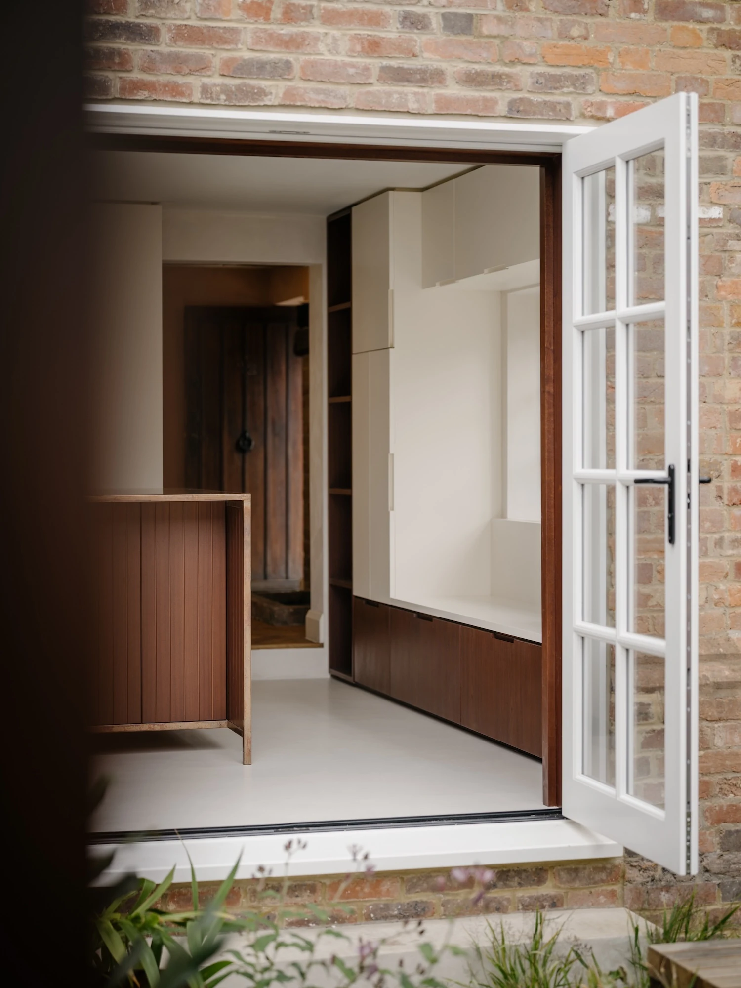 Muttram Veedu by Will Gamble Architects, photographed by James Retief — White French doors open from the courtyard into the kitchen, a sapele island and polished concrete floor beyond.