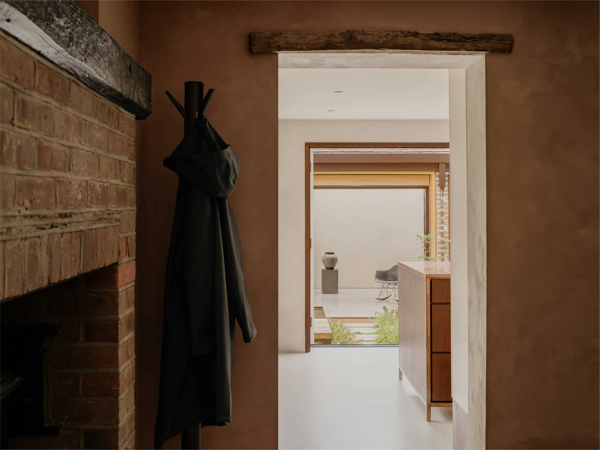 Muttram Veedu by Will Gamble Architects, photographed by James Retief — A passage in mottled, mud-plaster-toned paintwork opens toward the courtyard and the bright living room beyond.