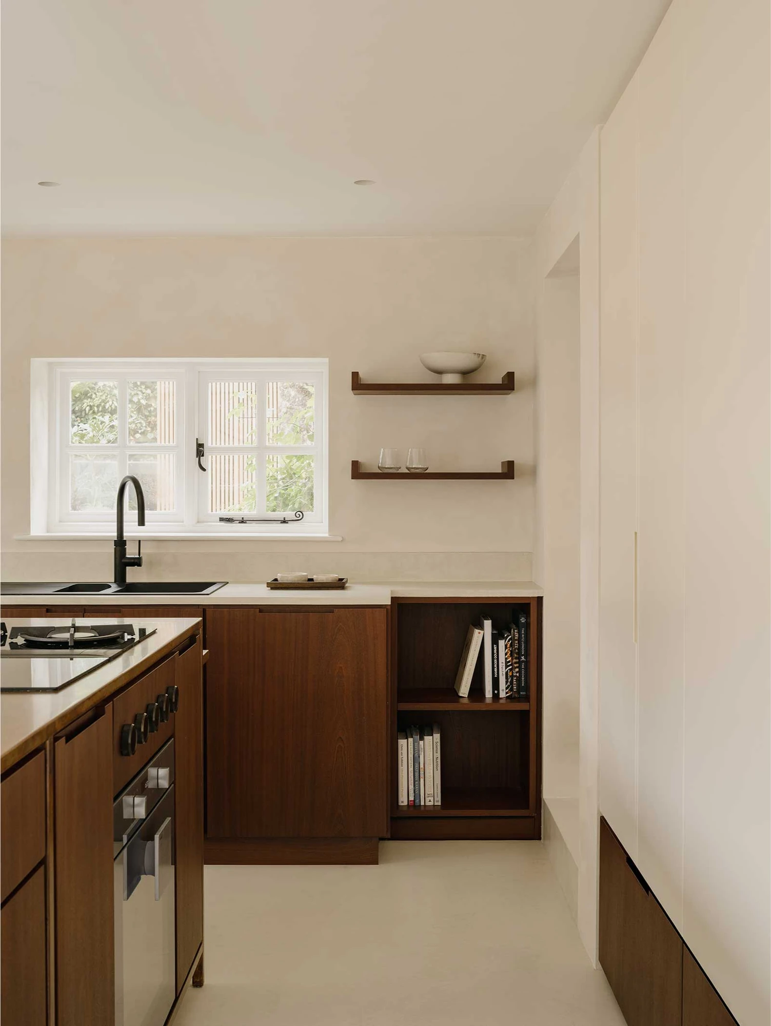 Muttram Veedu by Will Gamble Architects, photographed by James Retief — A black tap and sink sit below a cottage casement window, sapele cabinets and open shelves alongside on polished concrete.