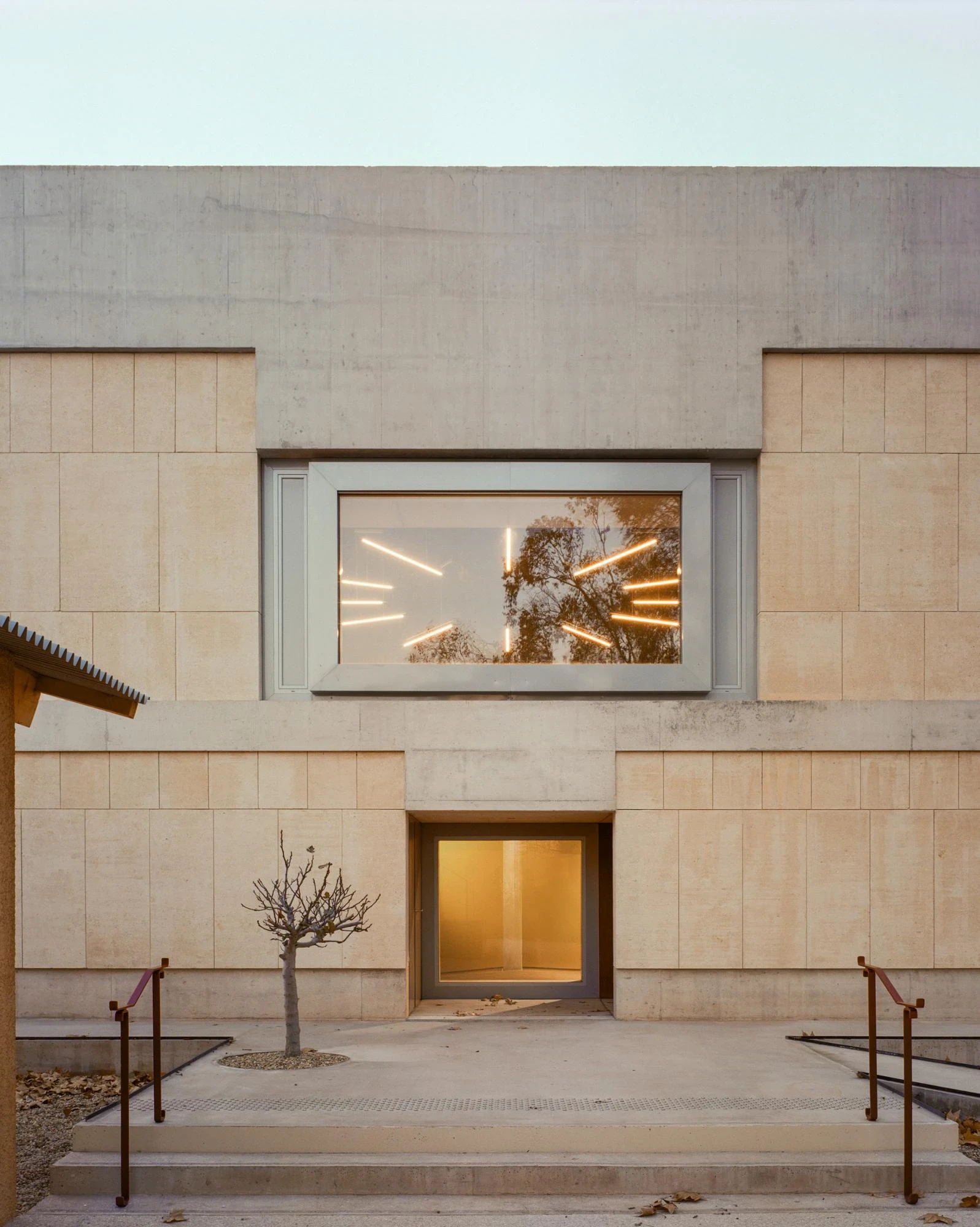 Cultural and Community Center, Coudoux by atelier EGR, photographed by Giaime Meloni — Stone cladding meets raw concrete at the entrance to the main building, a young tree in the forecourt.