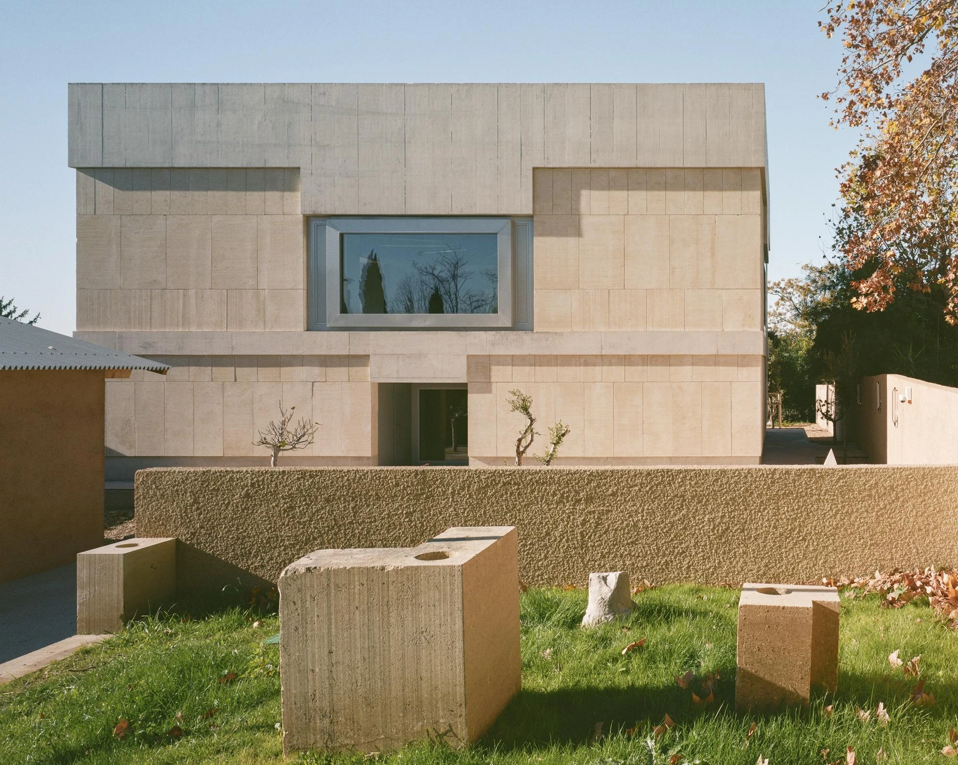 Cultural and Community Center, Coudoux by atelier EGR, photographed by Giaime Meloni — The main building rises in load-bearing stone above a raw concrete base, cut blocks set on the grass before it.