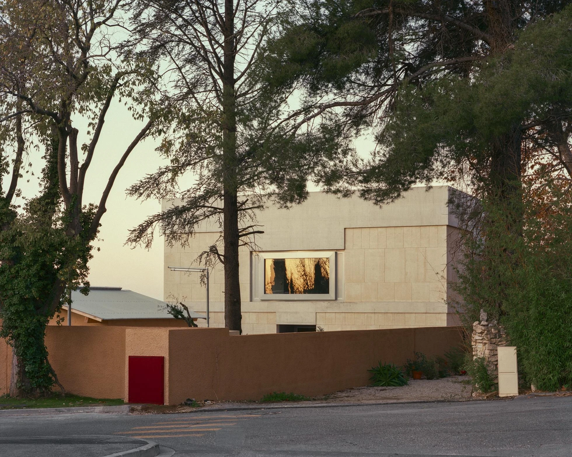 Cultural and Community Center, Coudoux by atelier EGR, photographed by Giaime Meloni — At dusk the main building stands behind trees along the street, its stone reading pale against the sky.