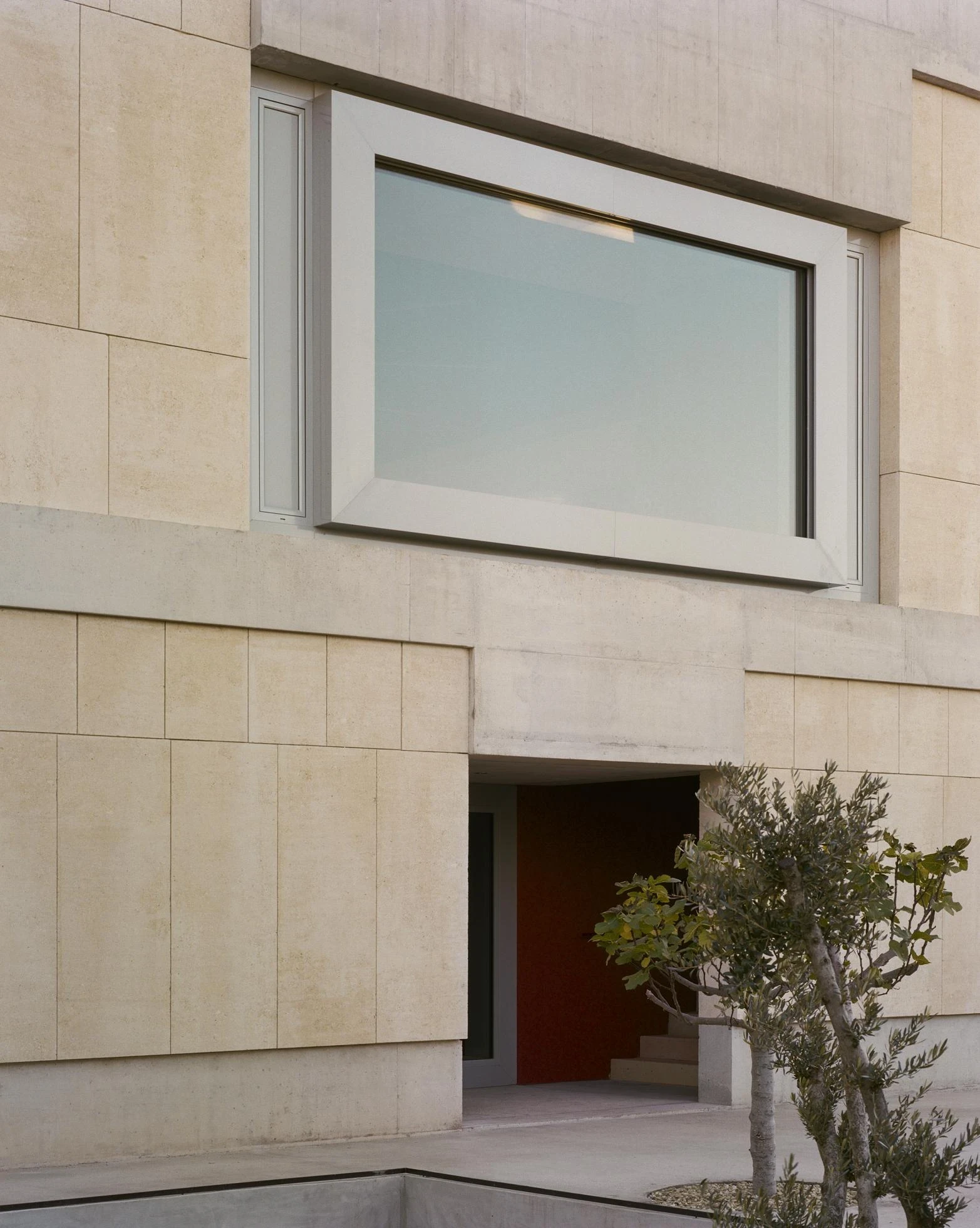 Cultural and Community Center, Coudoux by atelier EGR, photographed by Giaime Meloni — A thick fixed window frame sits above the entrance, where red earth plaster lines the space within.