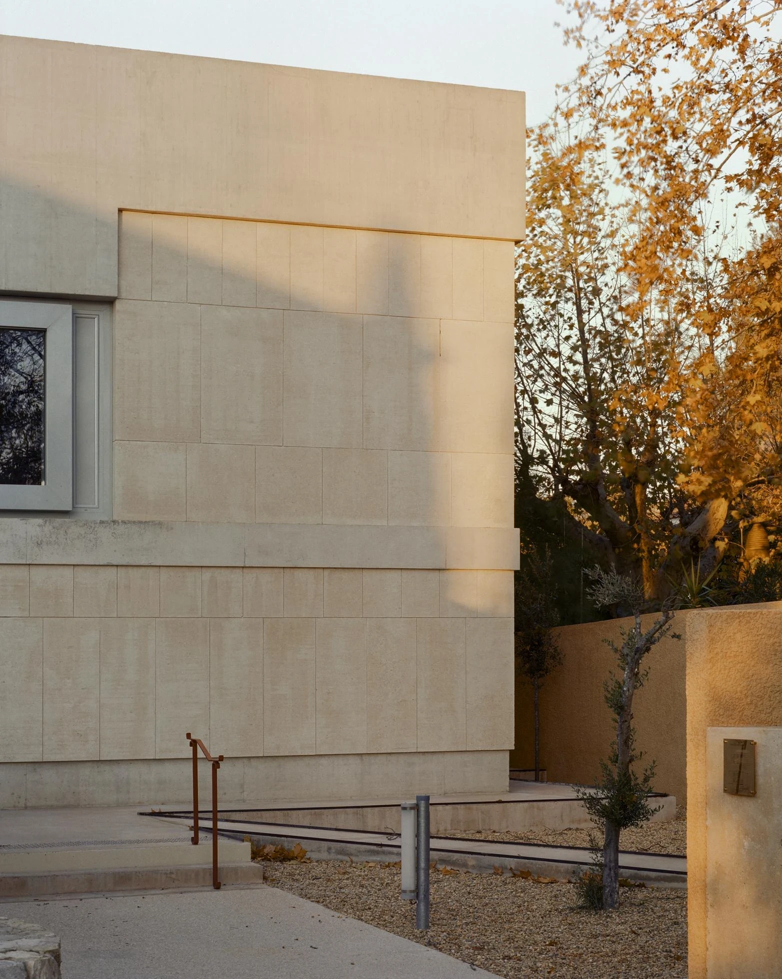 Cultural and Community Center, Coudoux by atelier EGR, photographed by Giaime Meloni — A deep-set window punctuates the stone facade of the main building beside a bare tree.