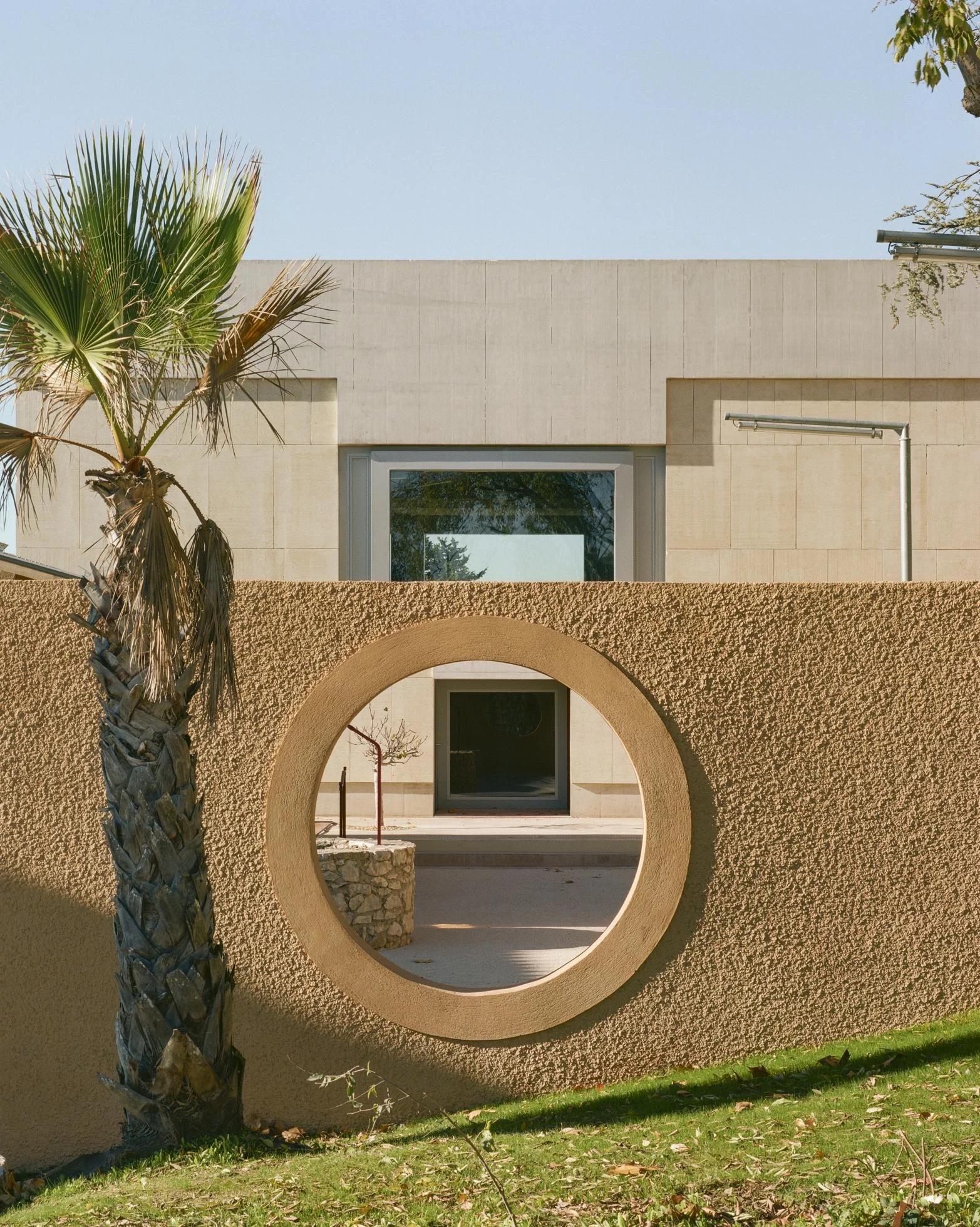 Cultural and Community Center, Coudoux by atelier EGR, photographed by Giaime Meloni — An oculus cut through the boundary wall frames the court and the old well beyond.