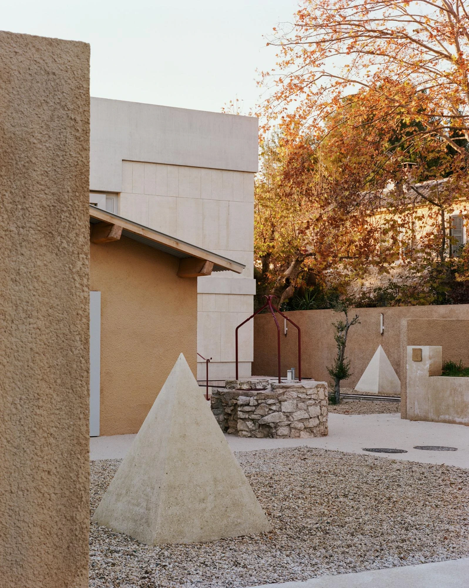 Cultural and Community Center, Coudoux by atelier EGR, photographed by Giaime Meloni — A stone pyramid and the old well share the square before the pitched-roof sheepfold.