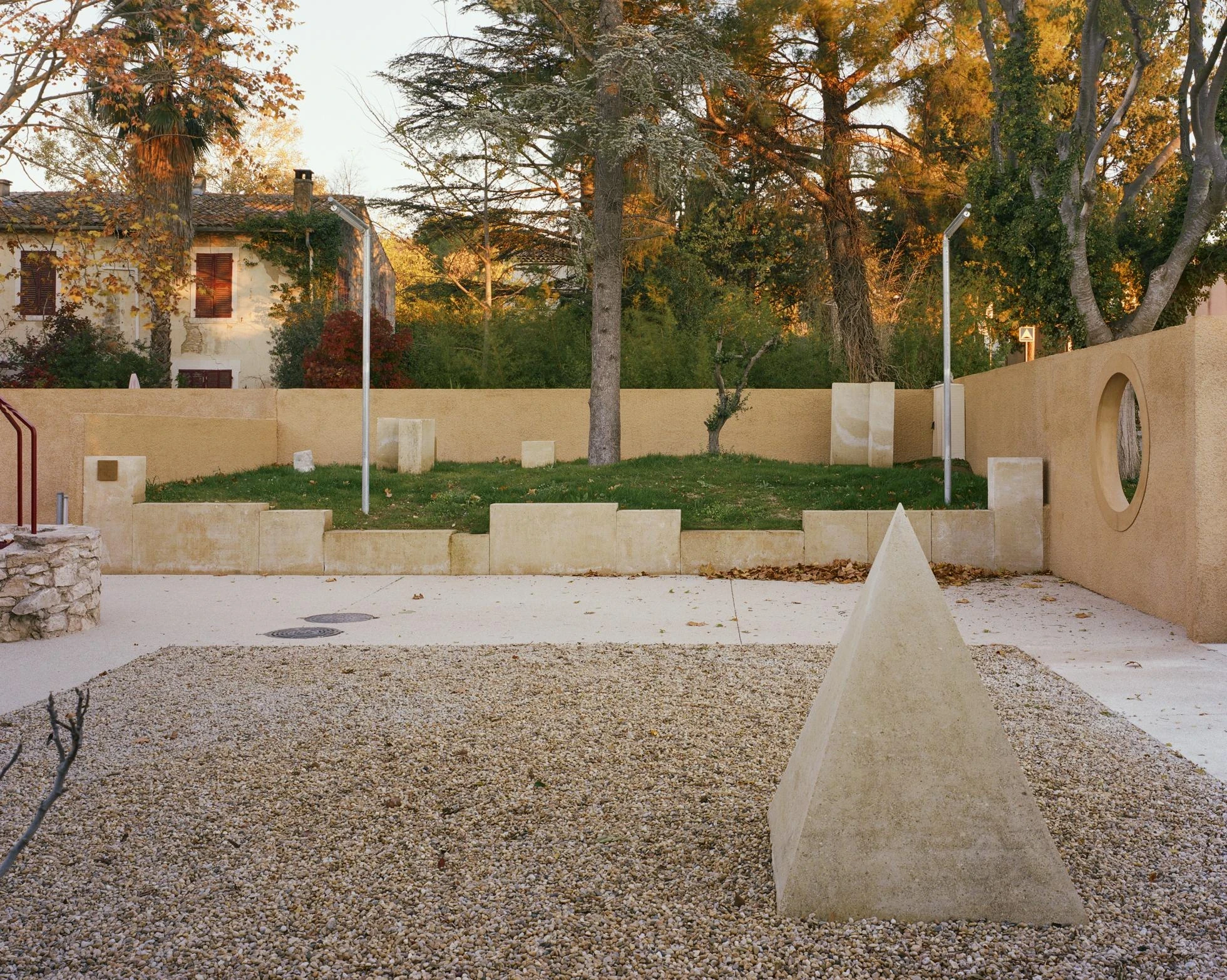 Cultural and Community Center, Coudoux by atelier EGR, photographed by Giaime Meloni — Stone pyramids, the old well and an oculus in the boundary wall order the square around a grassed mound.