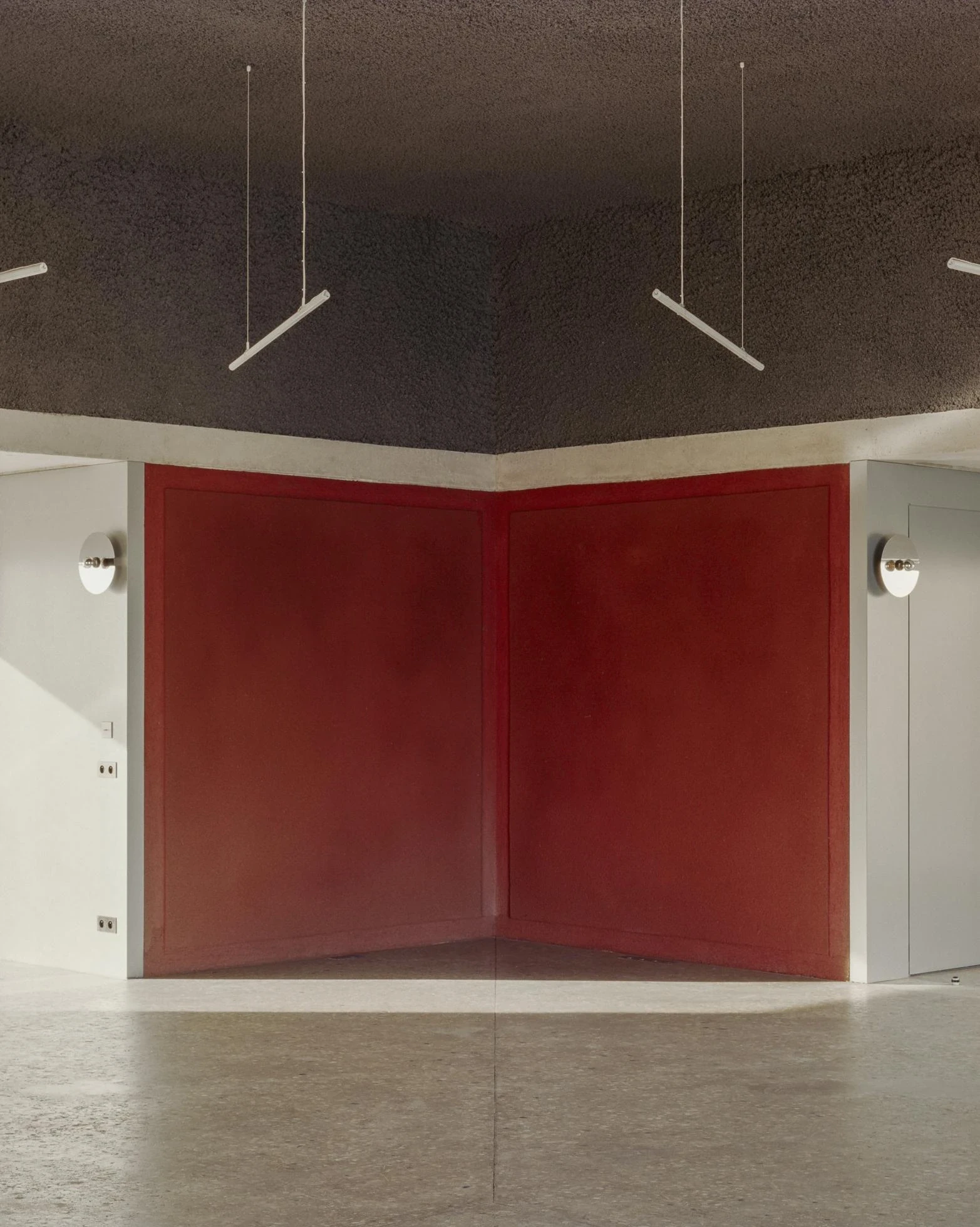Cultural and Community Center, Coudoux by atelier EGR, photographed by Giaime Meloni — Two planes of red earth plaster meet at a corner on the ground floor beneath a raw concrete beam.