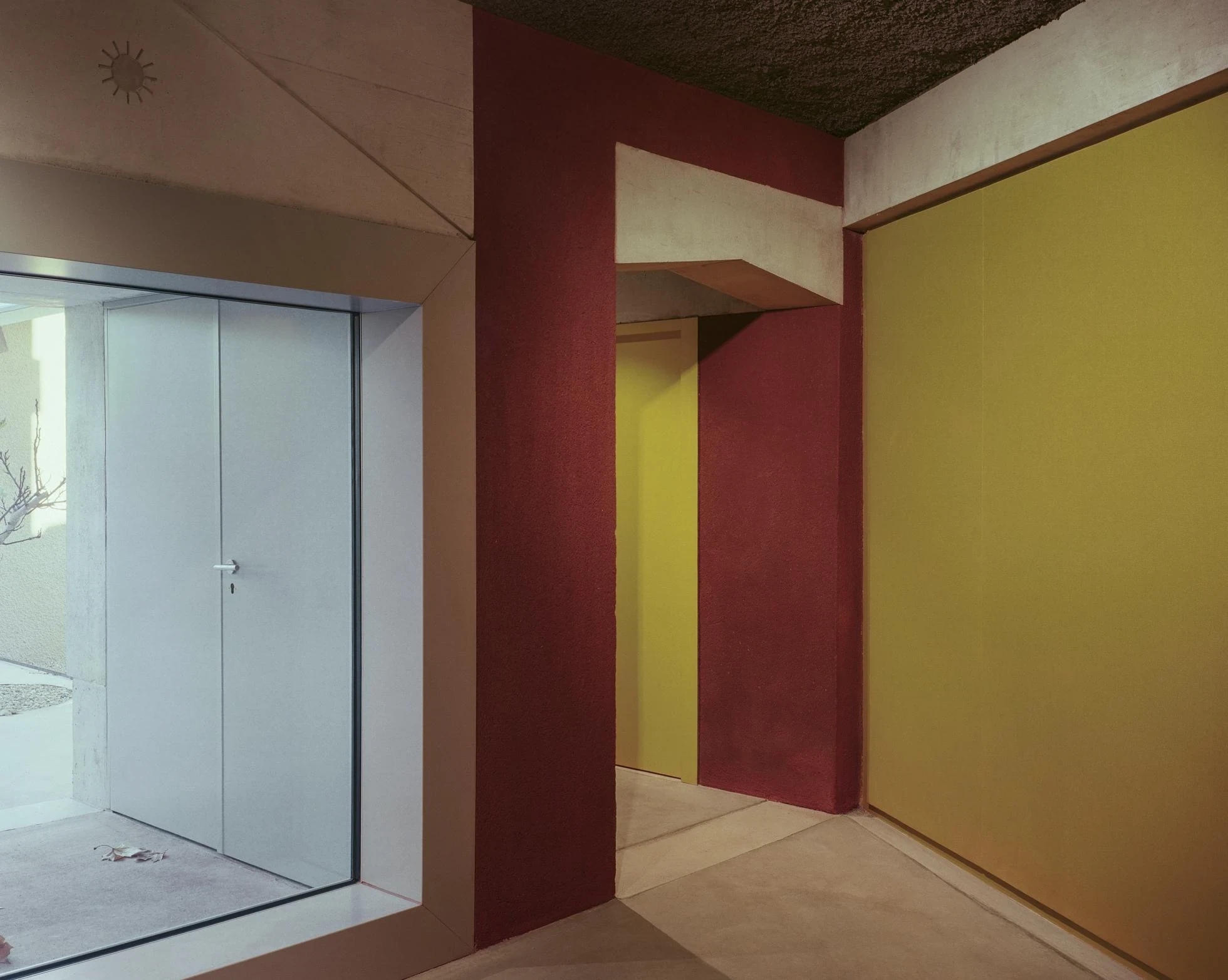 Cultural and Community Center, Coudoux by atelier EGR, photographed by Giaime Meloni — Walls of red earth plaster meet a yellow surface at a raw concrete opening, a glazed door onto the court beyond.