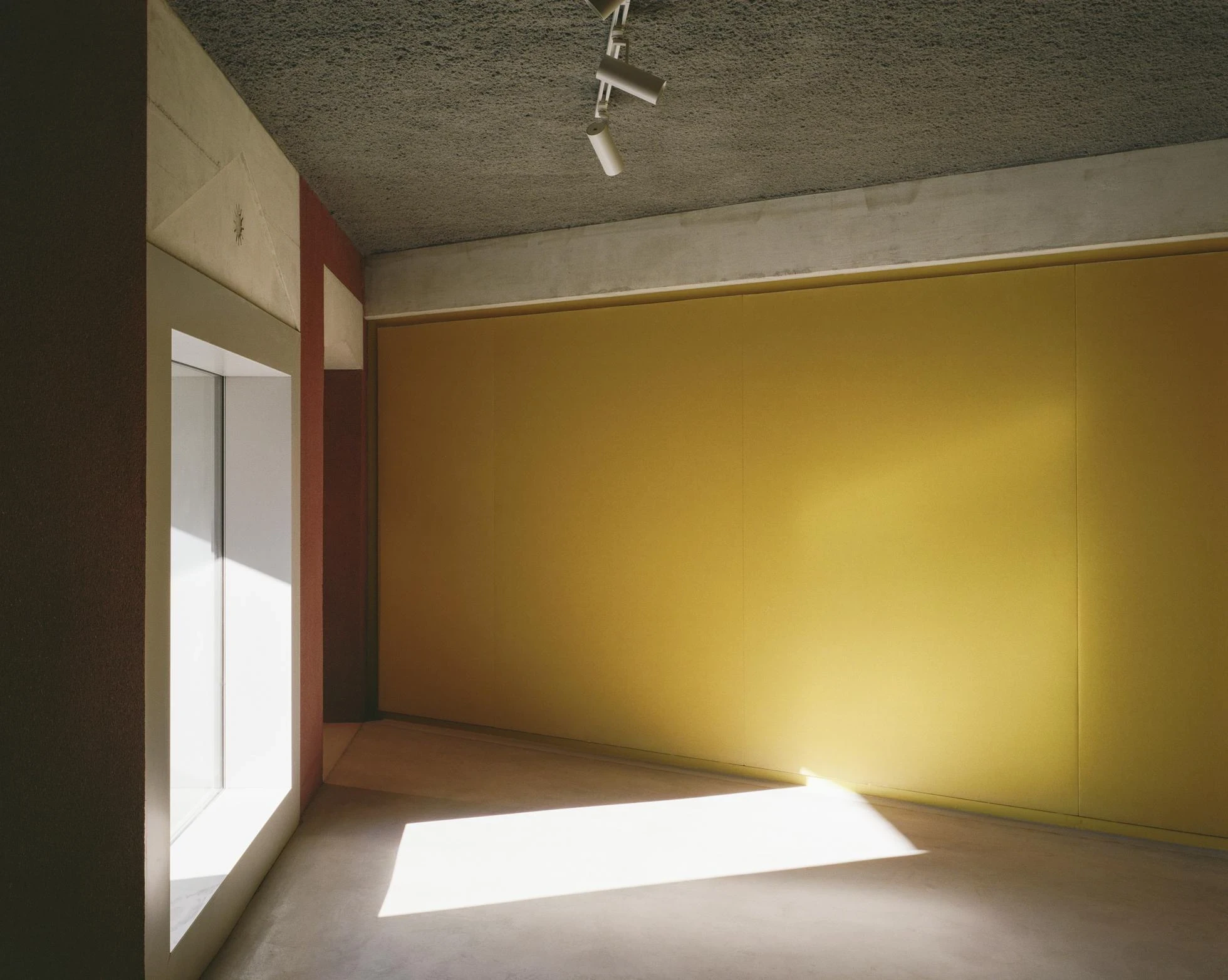 Cultural and Community Center, Coudoux by atelier EGR, photographed by Giaime Meloni — Sunlight crosses the concrete floor toward a wall of yellow acoustic fabric.