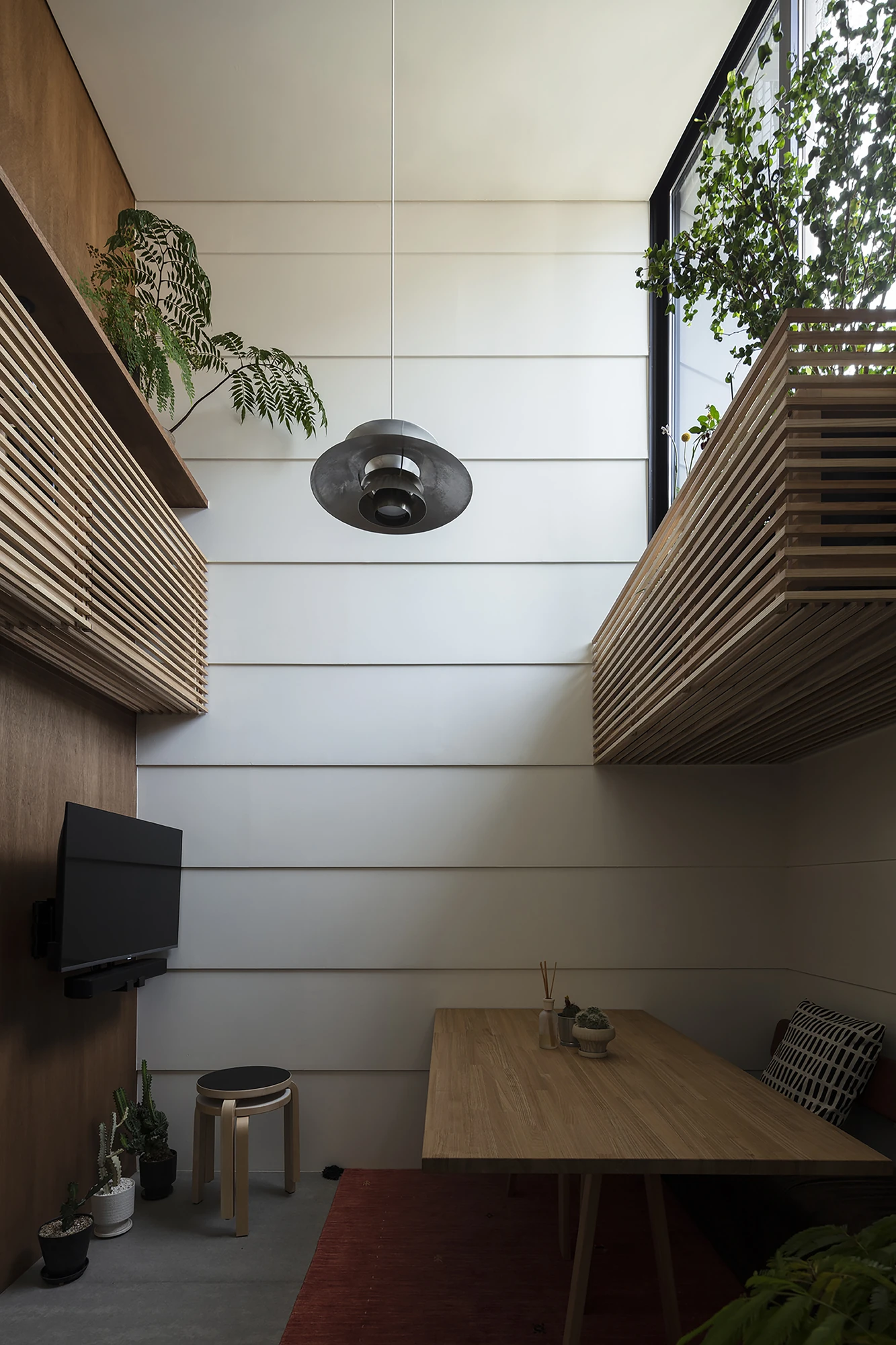 House in Kagurazaka by Takumi Wakui + Riho Wakui Architects — Framed windows carry greenery into the double-height living room, its walls lined in timber under the curved edge of the void.