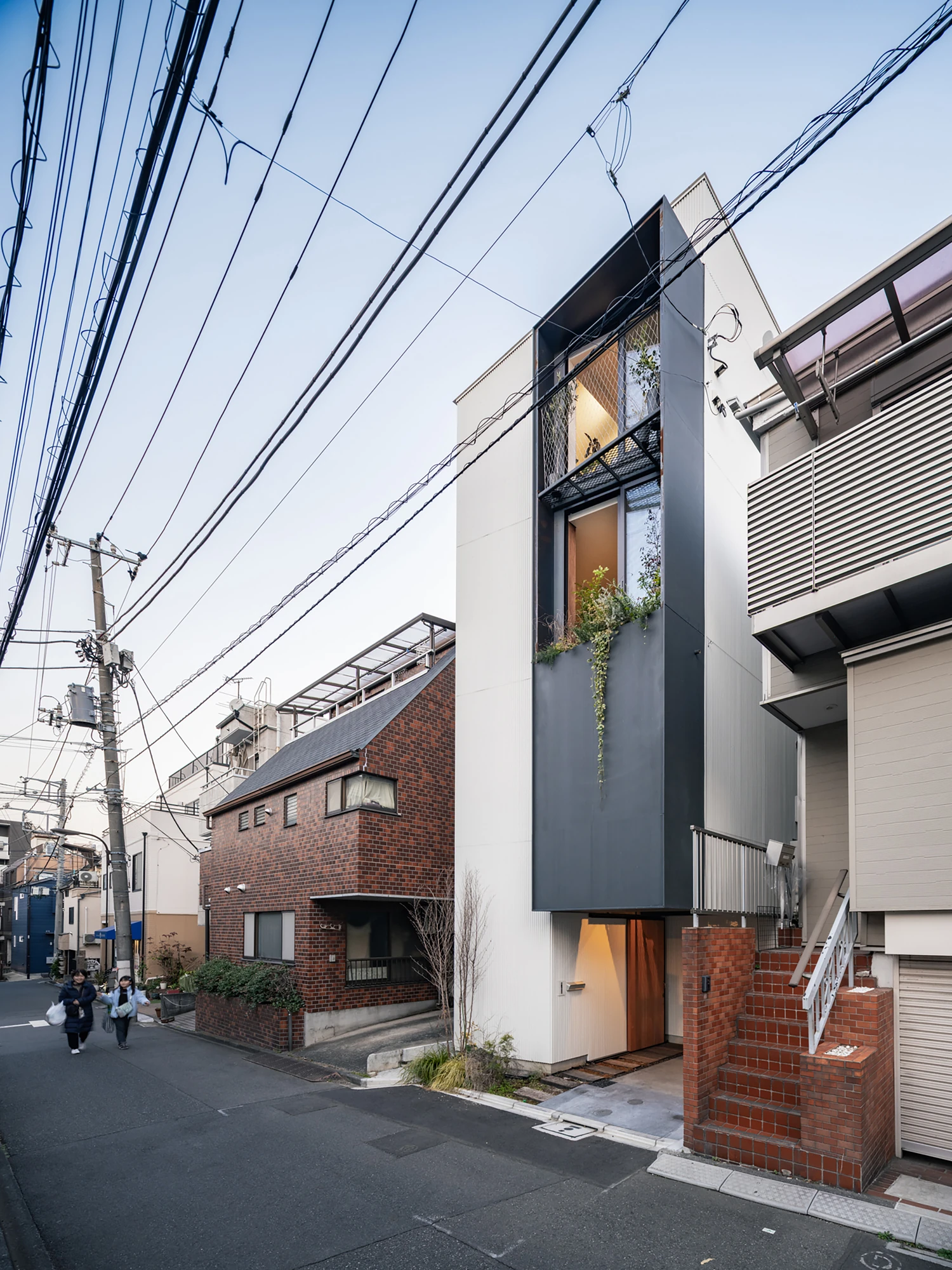 House in Kagurazaka by Takumi Wakui + Riho Wakui Architects — Seen along the street, the slender timber-structure volume steps up four storeys, framed windows opening to greenery above the entrance.