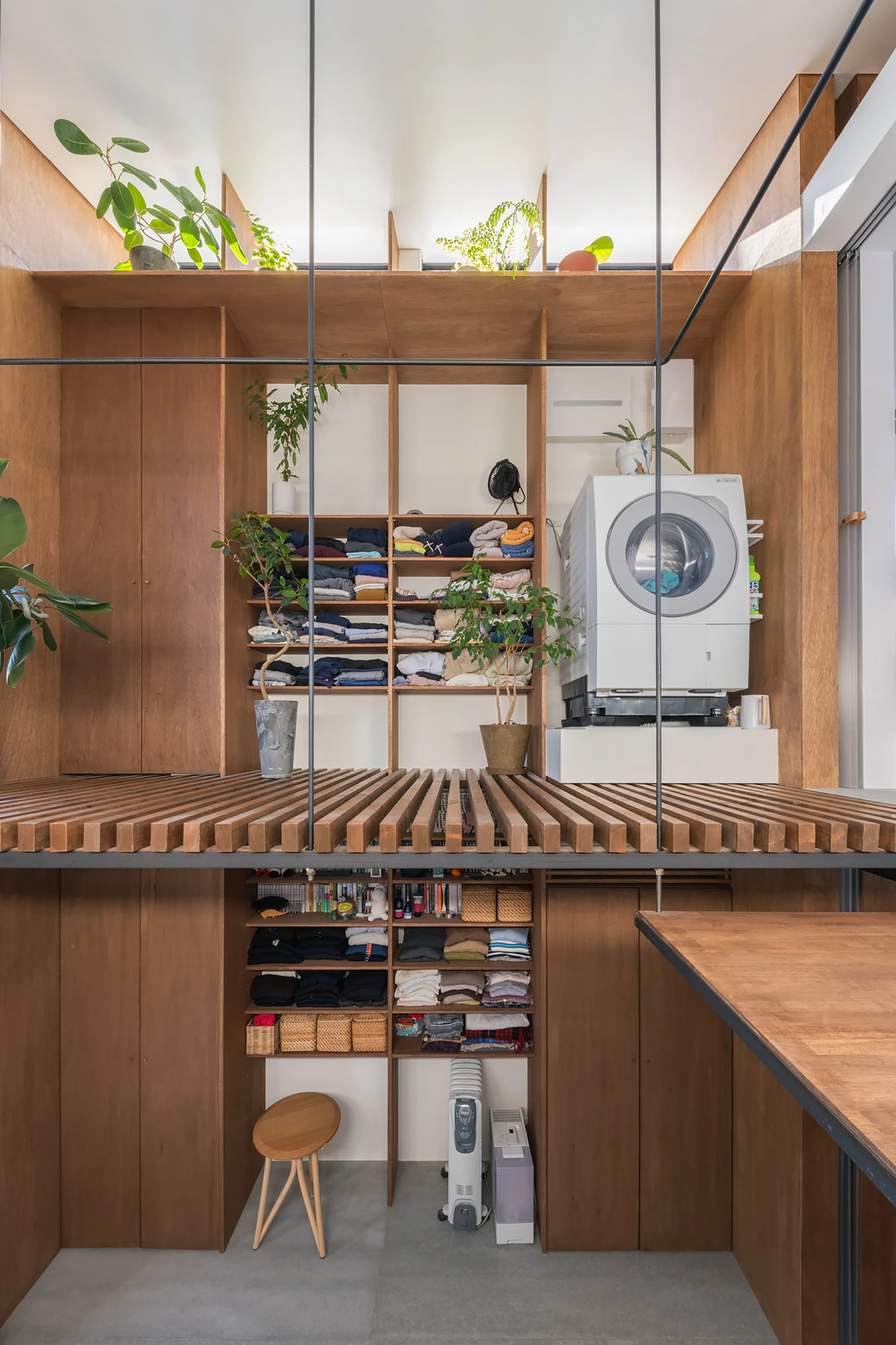 House in Kagurazaka by Takumi Wakui + Riho Wakui Architects — Open timber shelving and a slatted platform organise storage across a private upper floor, stacked within the multi-storey void.