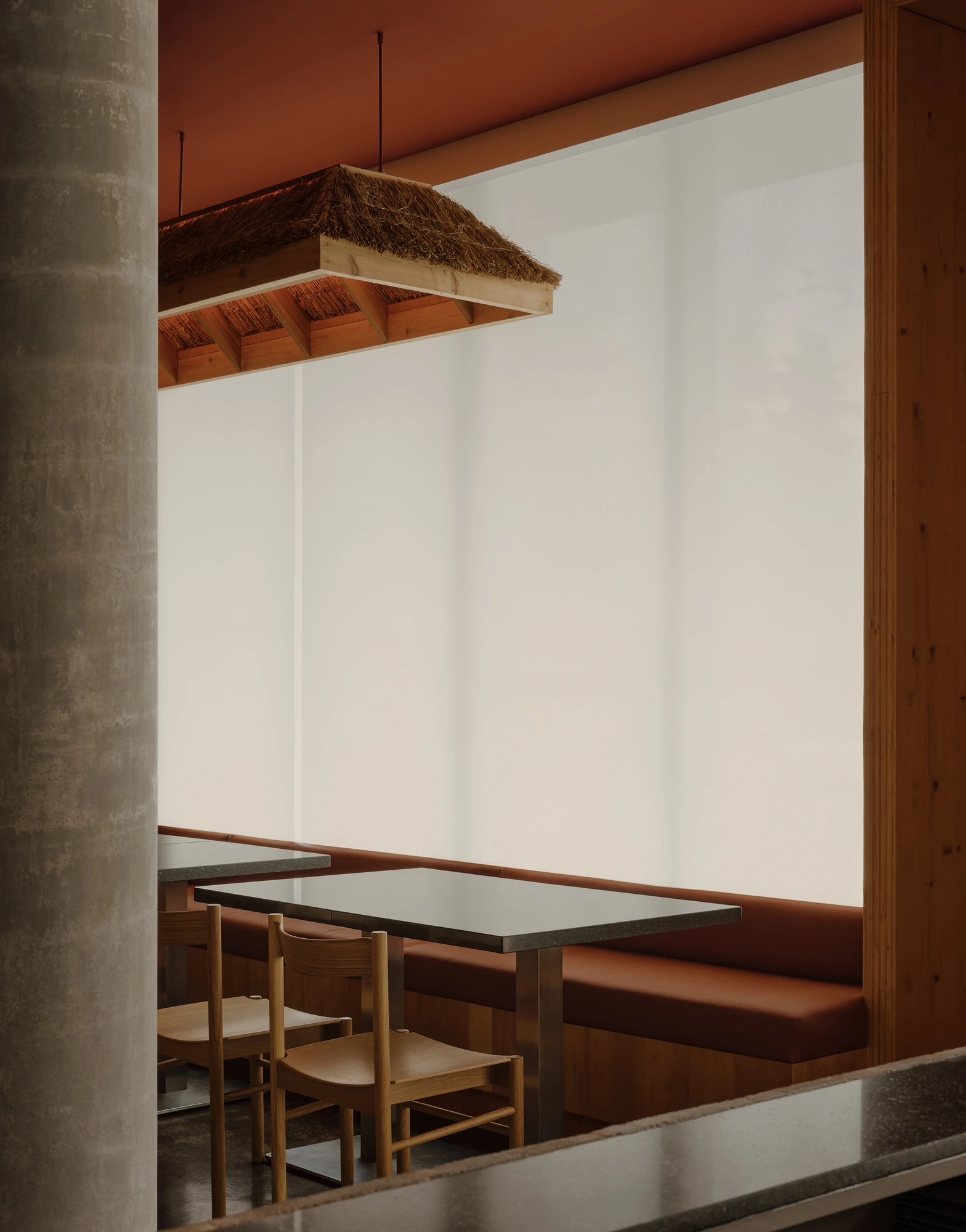 Jeju by &Daughters, photographed by Alex Lesage — A booth set into the cork wall, its backlit rectangular apertures scattered above the banquette, with a hand-thatched pendant and a carved stone figure nearby.