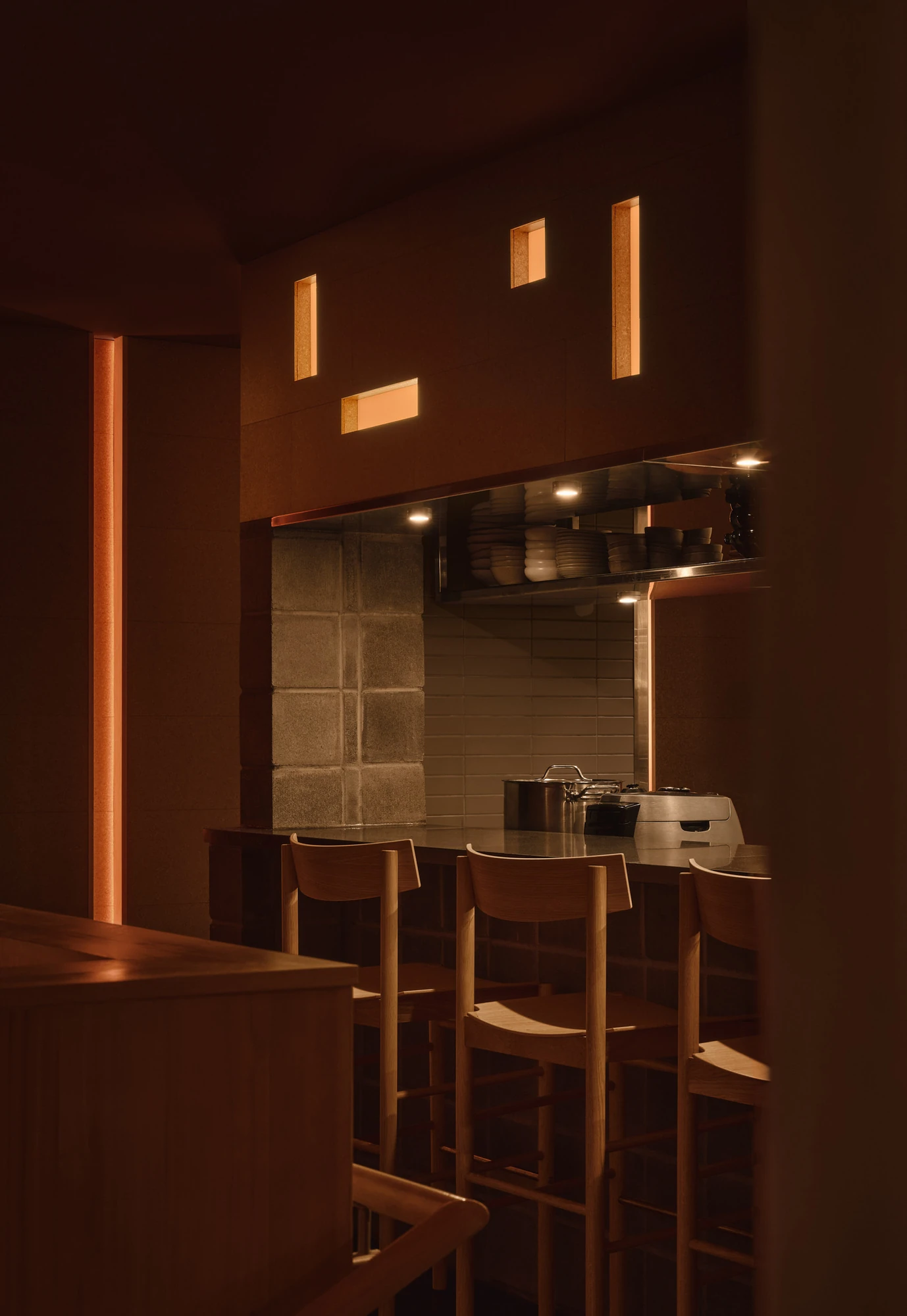 Jeju by &Daughters, photographed by Alex Lesage — A daytime view across the bar and dining room, with a concrete column, hand-thatched pendants and backlit apertures cut into the cork walls.