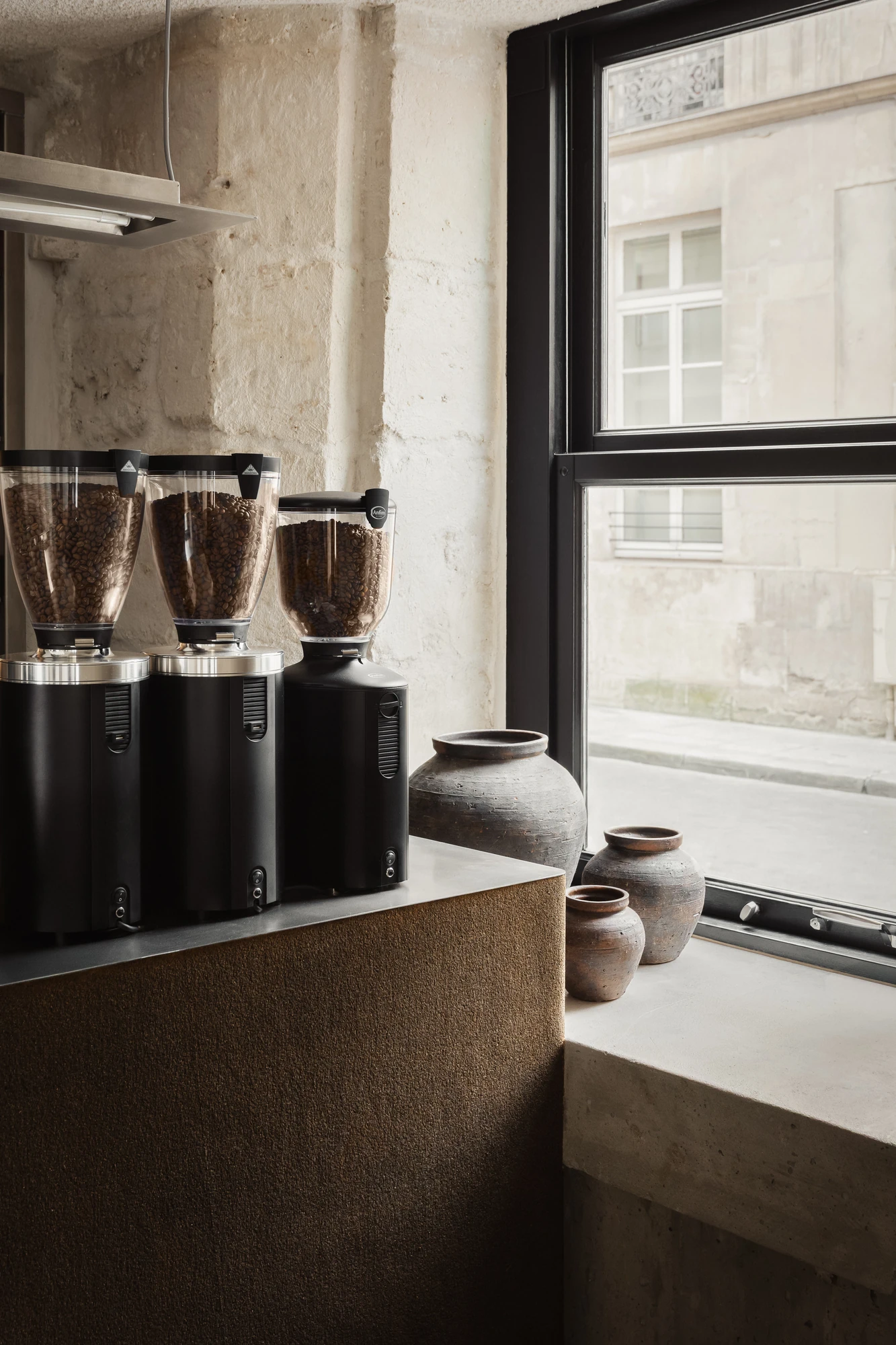 DAARK by Rodaa Studio, photographed by Adrien Ozouf — Coffee grinders on the counter beside a window inside DAARK, rue de Turenne, Paris.