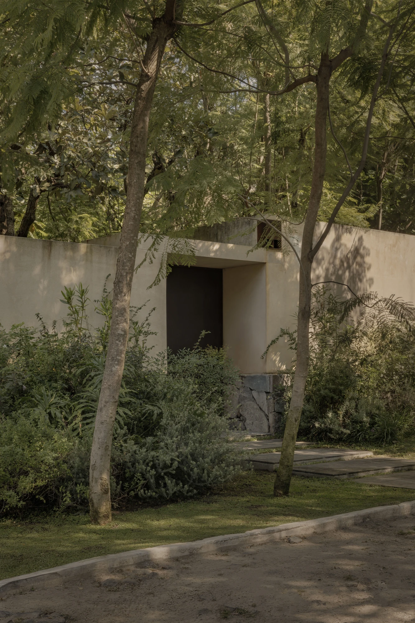 PRM39 by Ana Victoria Pérez-Gil | Saúl Figueroa, photographed by Funciono — A path of stone slabs leads through endemic planting to an opening in the stucco wall of the house.