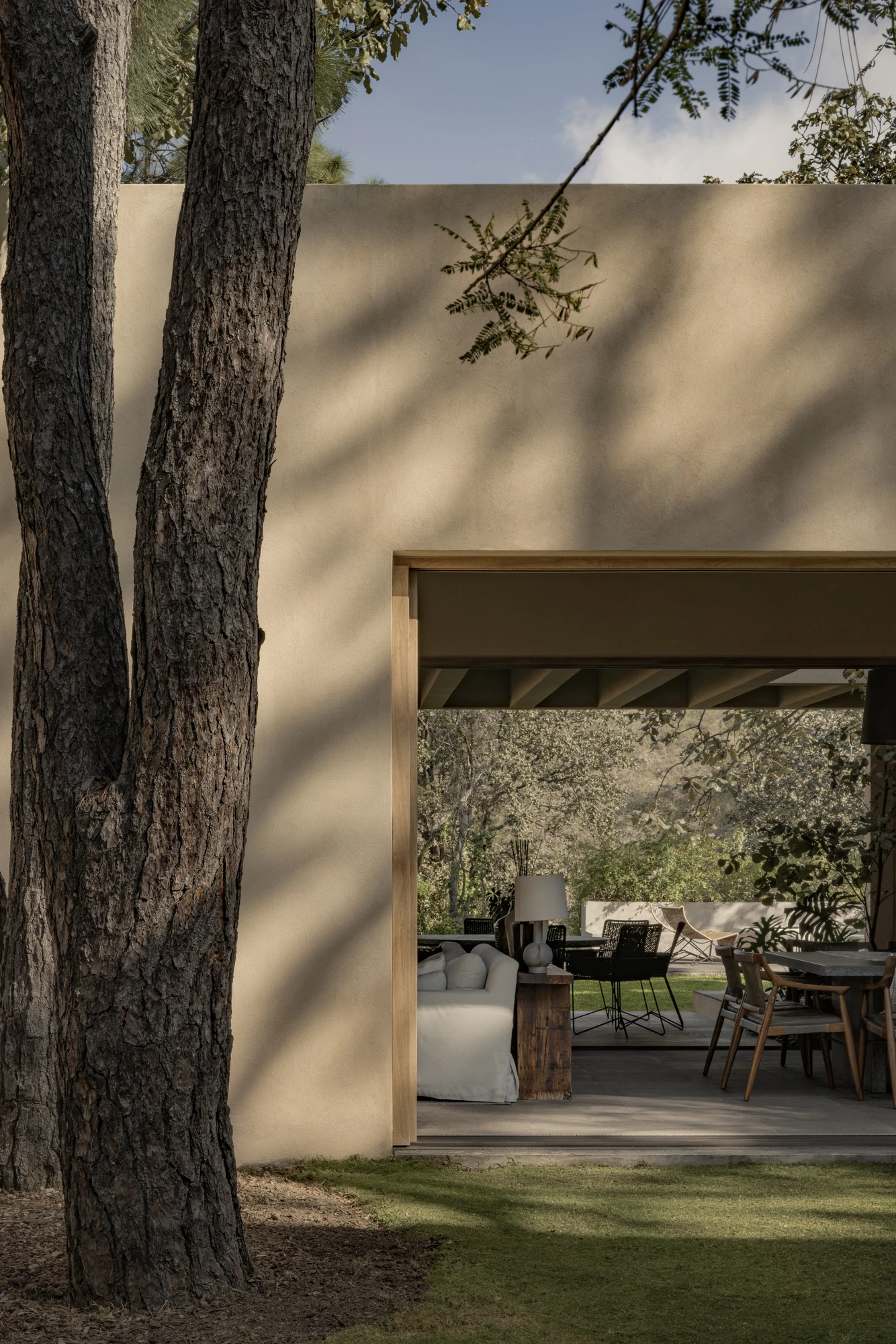 PRM39 by Ana Victoria Pérez-Gil | Saúl Figueroa, photographed by Funciono — A tree trunk stands before an opening in the stucco wall, the living spaces of PRM39 beyond.