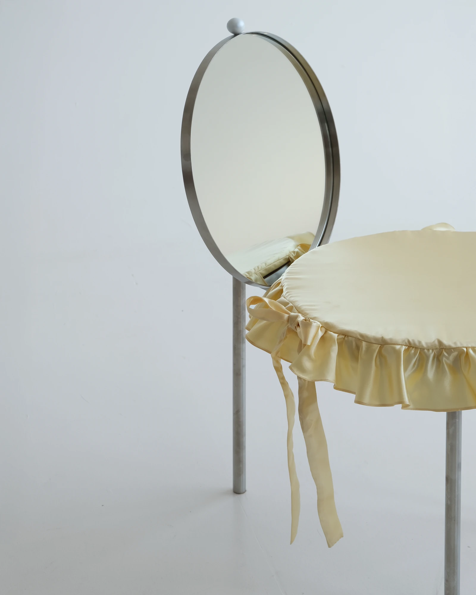The Woman's Chair by Shushana Khachatrian, photographed by Katie Kutuzova — Three-quarter view of the frilled satin cushion and round mirror backrest raised on slender stainless-steel legs.
