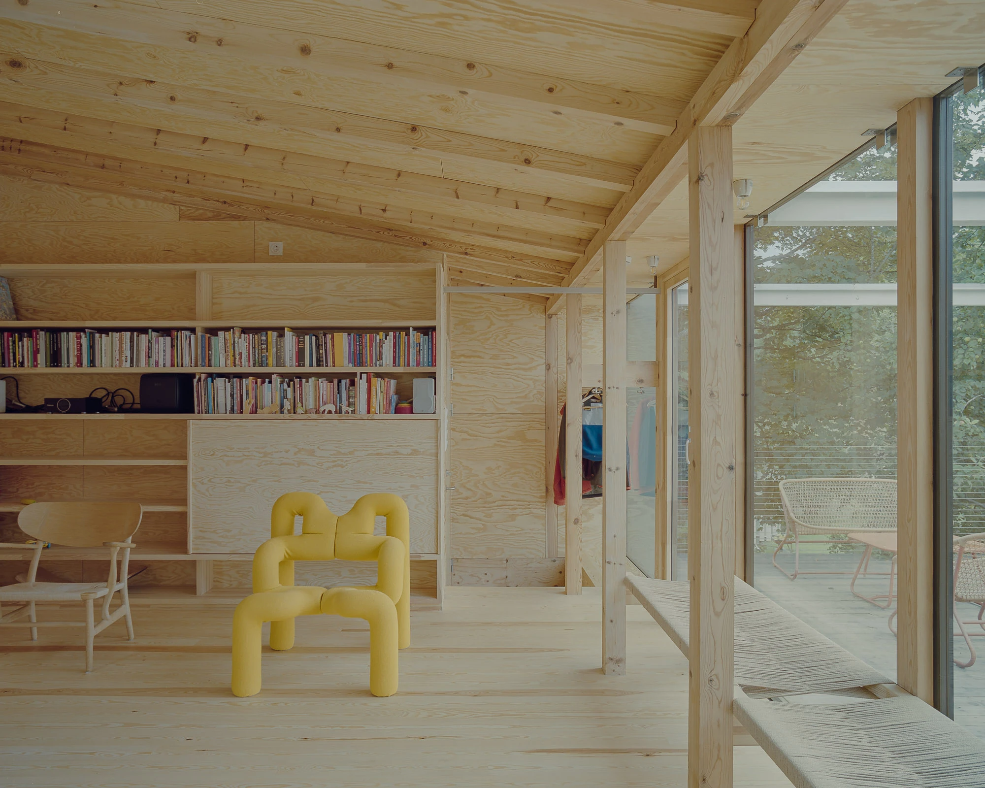 Ersland & Skeie House by Knut Hjeltnes Architects, photographed by Hugo Lütcherath — Pine post and beam frames a living space lined in peeled pine plywood, opening through full-height glass to the piazzetta.