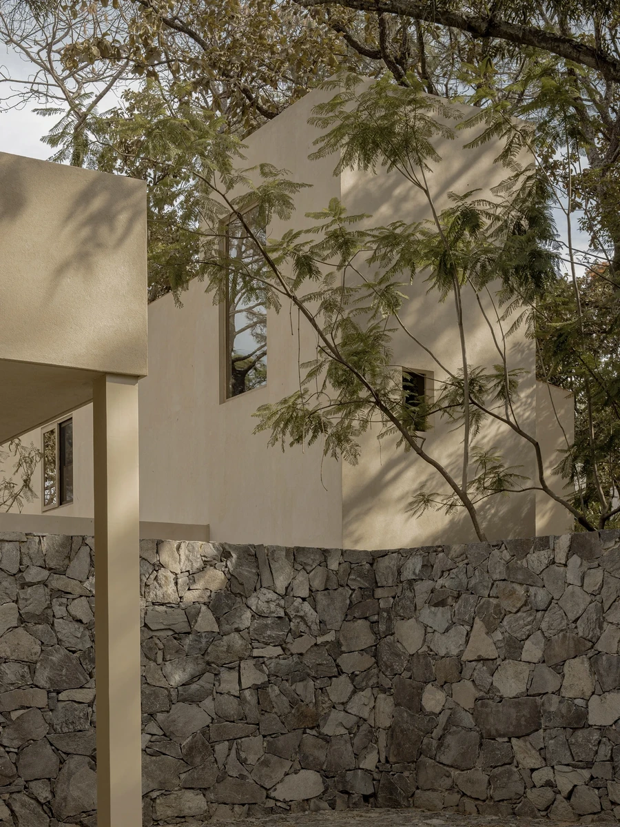 PRM39 by Ana Victoria Pérez-Gil | Saúl Figueroa, photographed by Funciono — A stucco volume of PRM39 meets a wood door where the house steps into the forest.