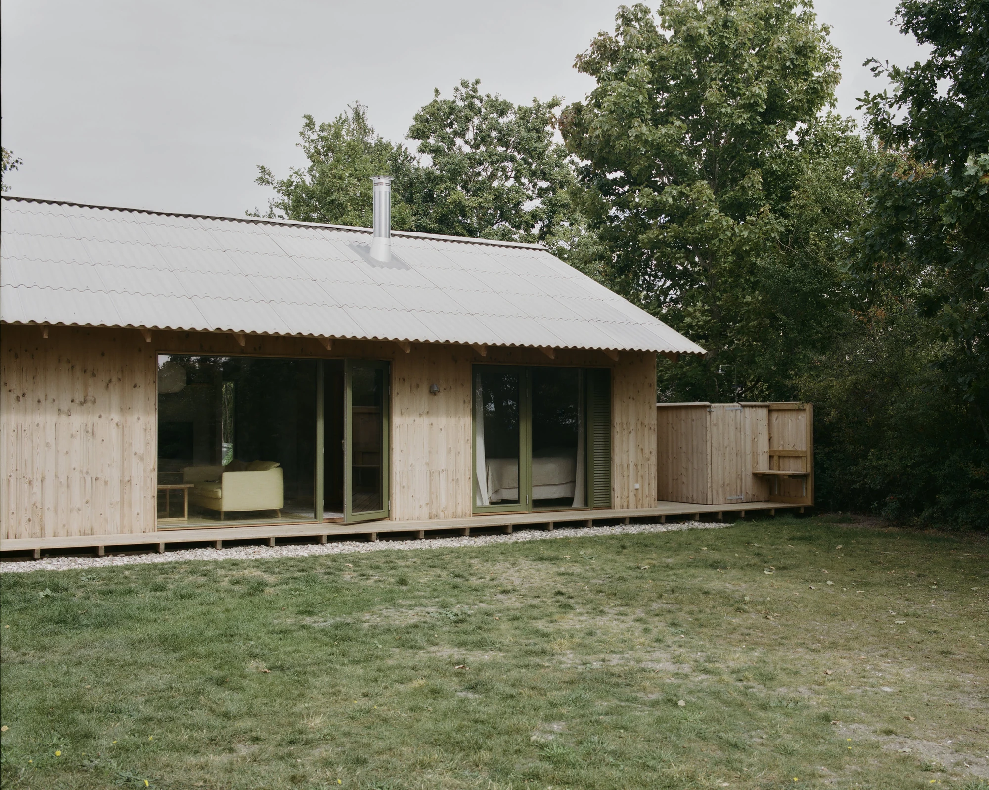 Stenkløvervej Vacation House by Studio Furö, photographed by Ditte Auguste Mørkholt — A three-quarter view of the house with a flue rising through the roof and a low store at the end of the deck.