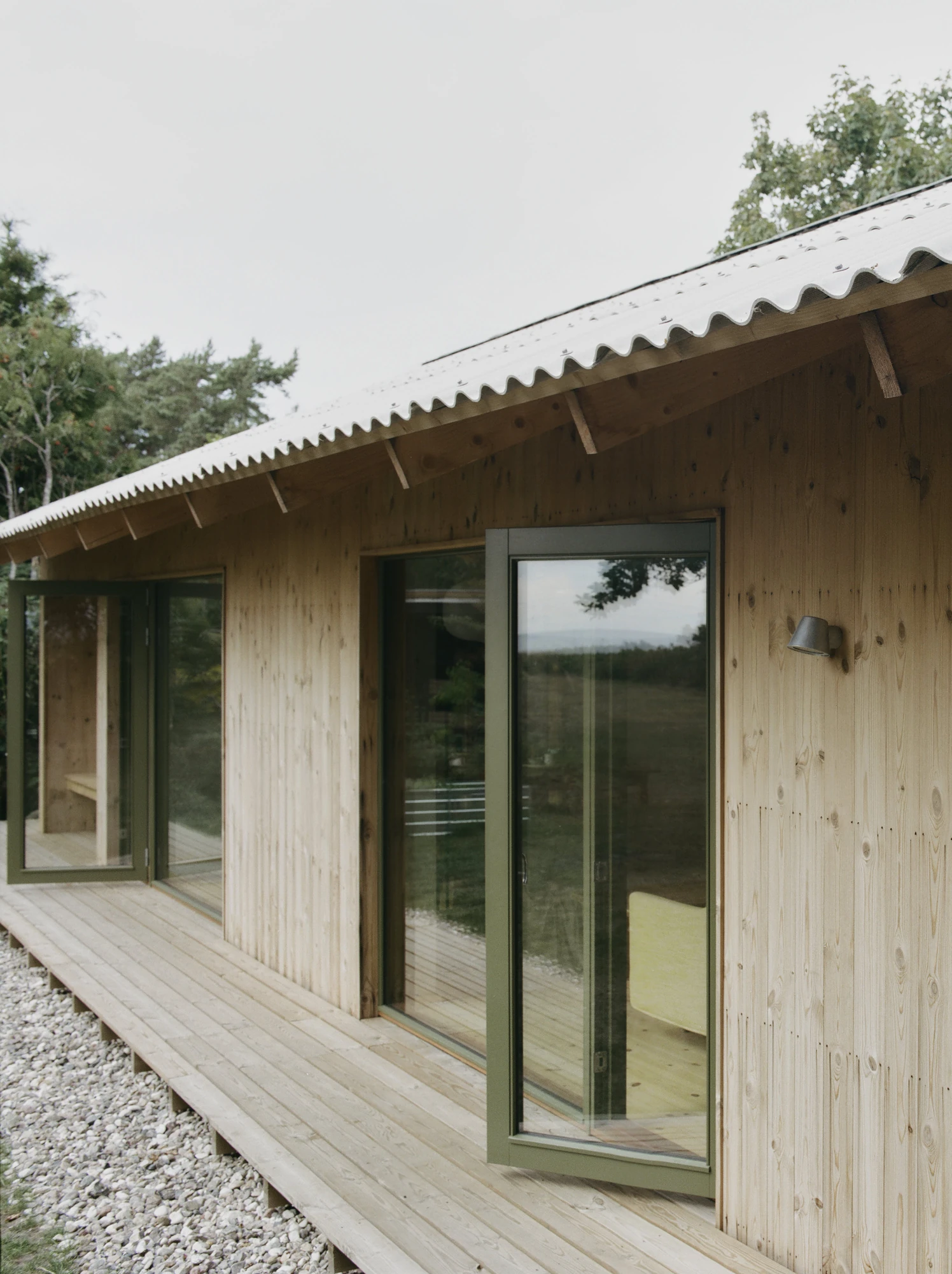 Stenkløvervej Vacation House by Studio Furö, photographed by Ditte Auguste Mørkholt — Doors and windows set along the deck, with the roof overhang carried on exposed rafters.