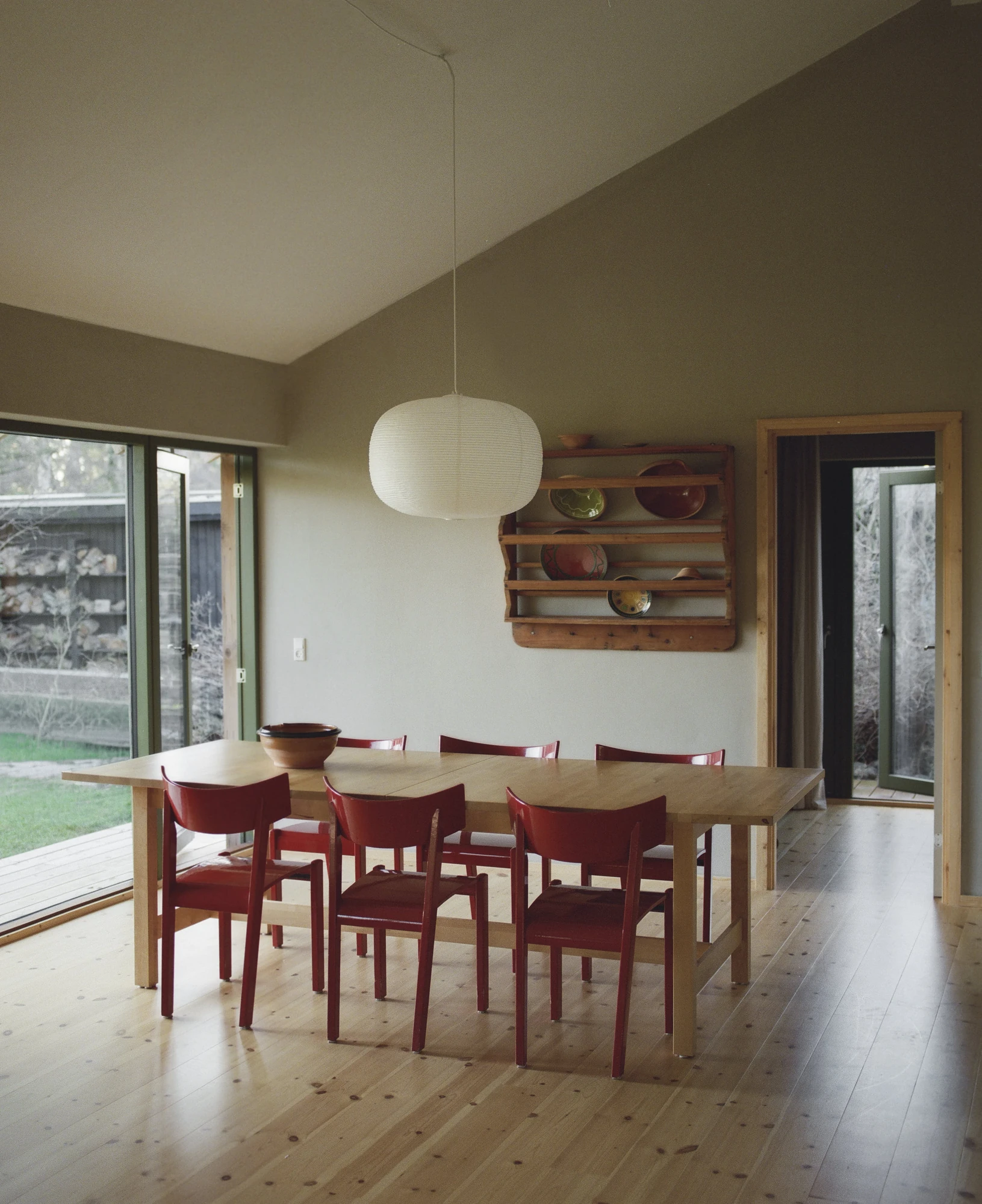 Stenkløvervej Vacation House by Studio Furö, photographed by Ditte Auguste Mørkholt — A dining table with chairs along both sides, a hanging lantern above it and a plate rack fixed to the wall.