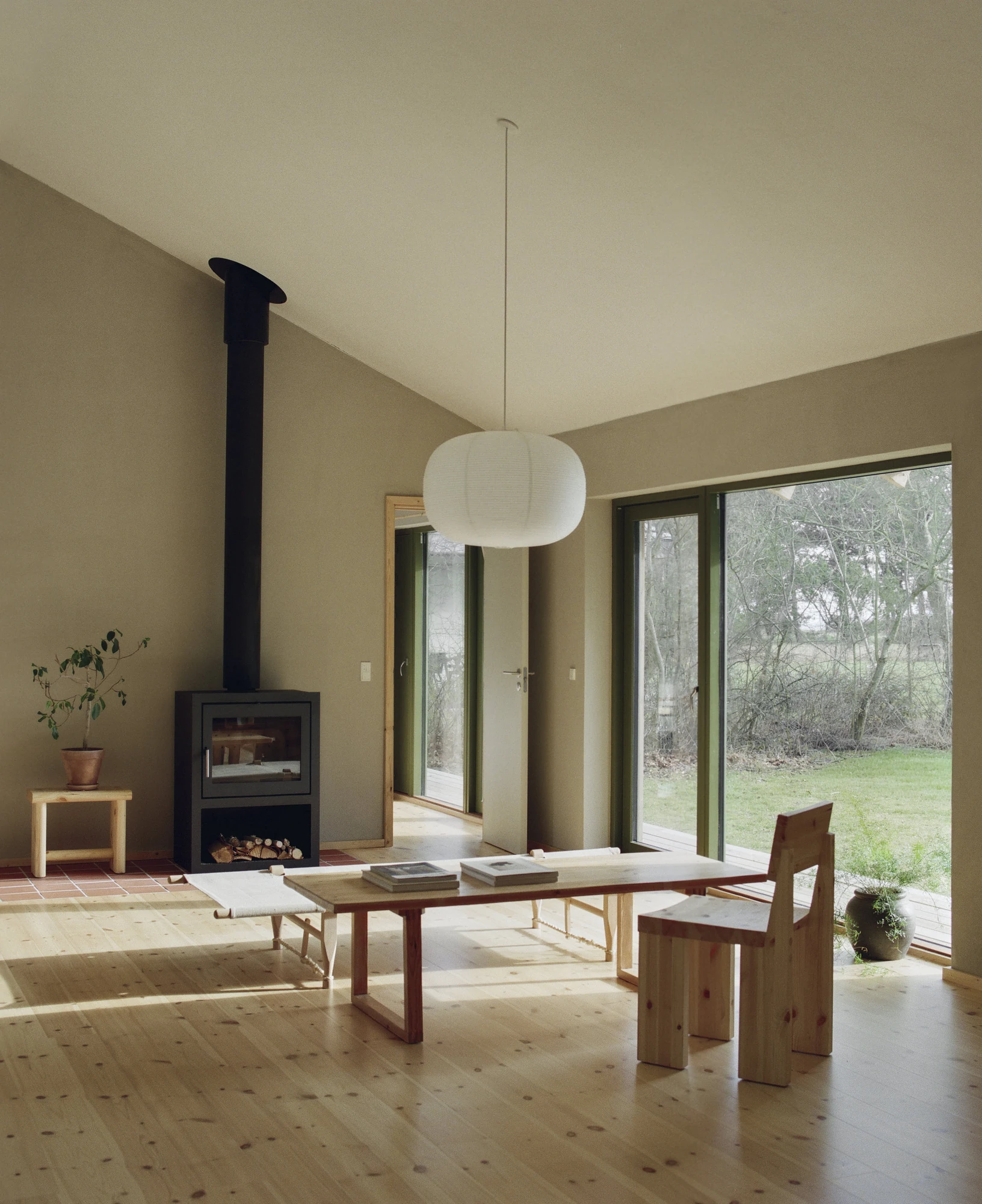 Stenkløvervej Vacation House by Studio Furö, photographed by Ditte Auguste Mørkholt — The living room with a wood-burning stove against the end wall, a paper lantern overhead and doors opening to the grass.