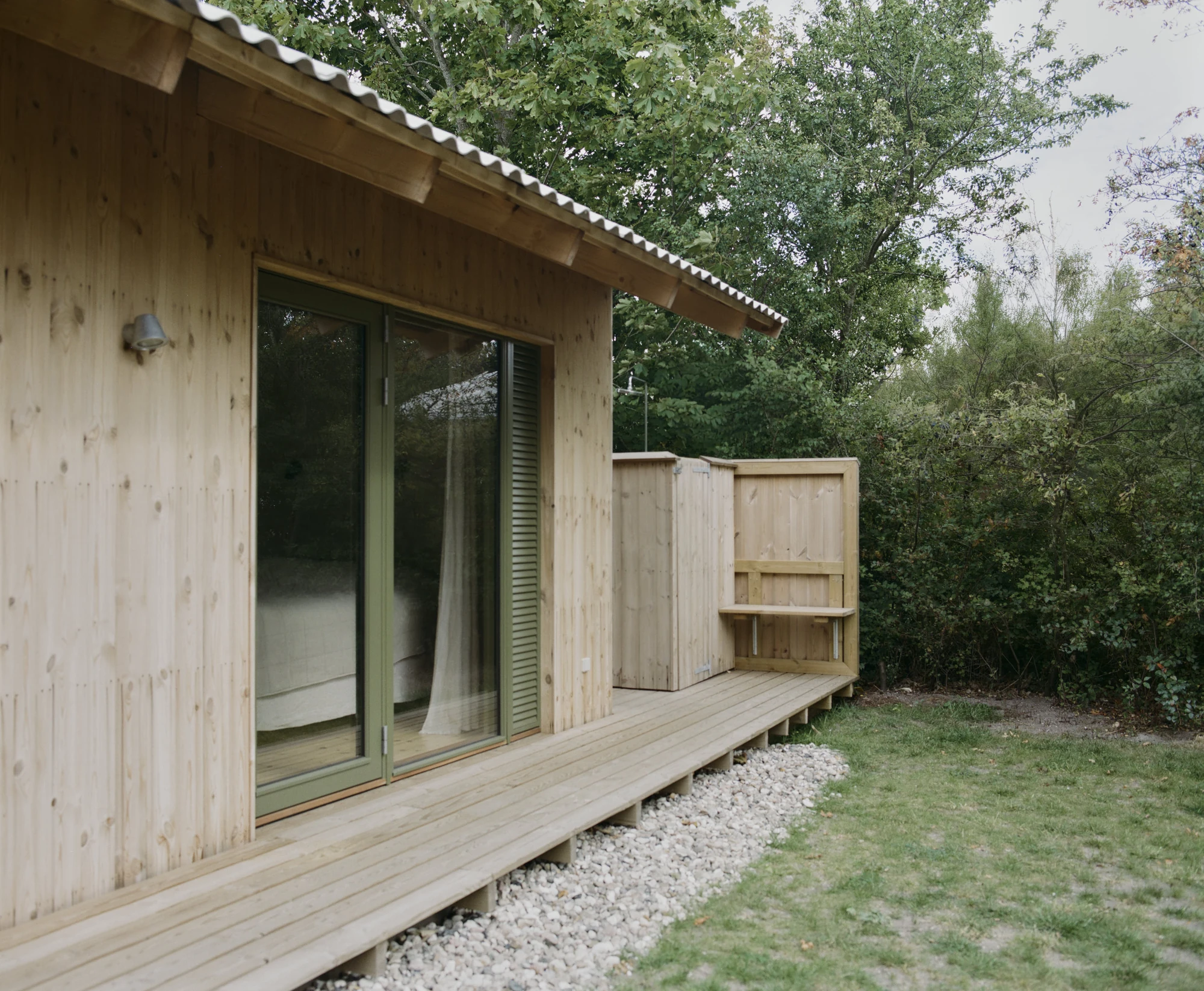 Stenkløvervej Vacation House by Studio Furö, photographed by Ditte Auguste Mørkholt — A sliding door opening from a bedroom onto the deck, with a screened enclosure and a shelf at the far end.