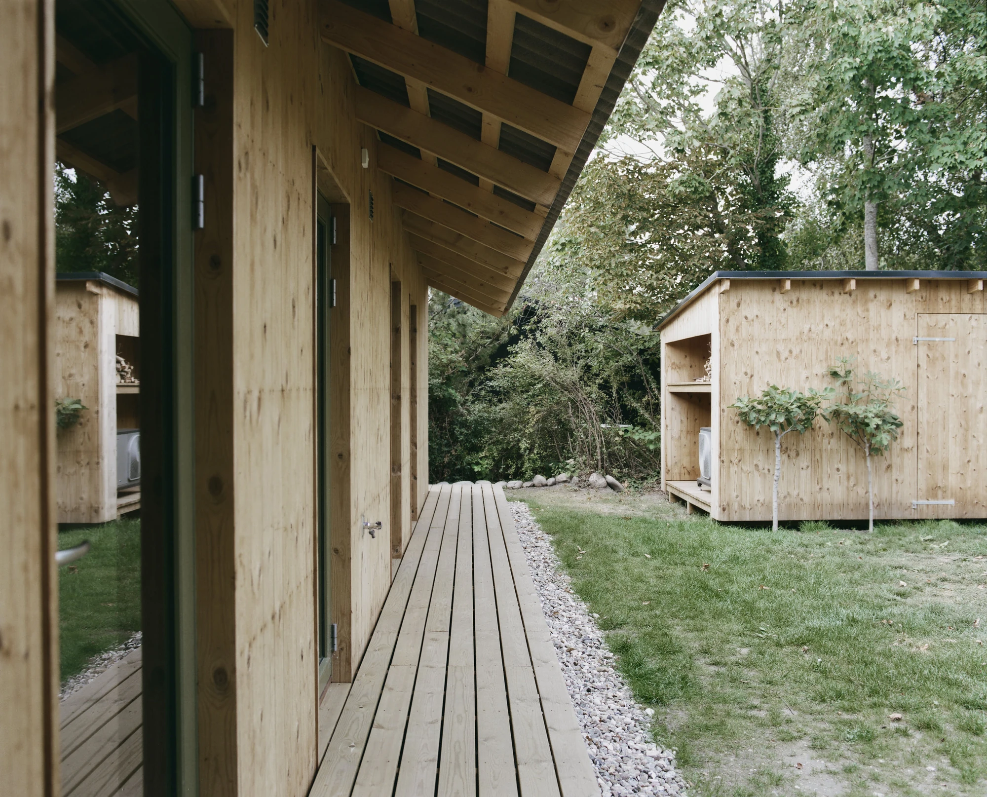 Stenkløvervej Vacation House by Studio Furö, photographed by Ditte Auguste Mørkholt — A walkway of boards running along the side of the house towards a separate store with open shelves.