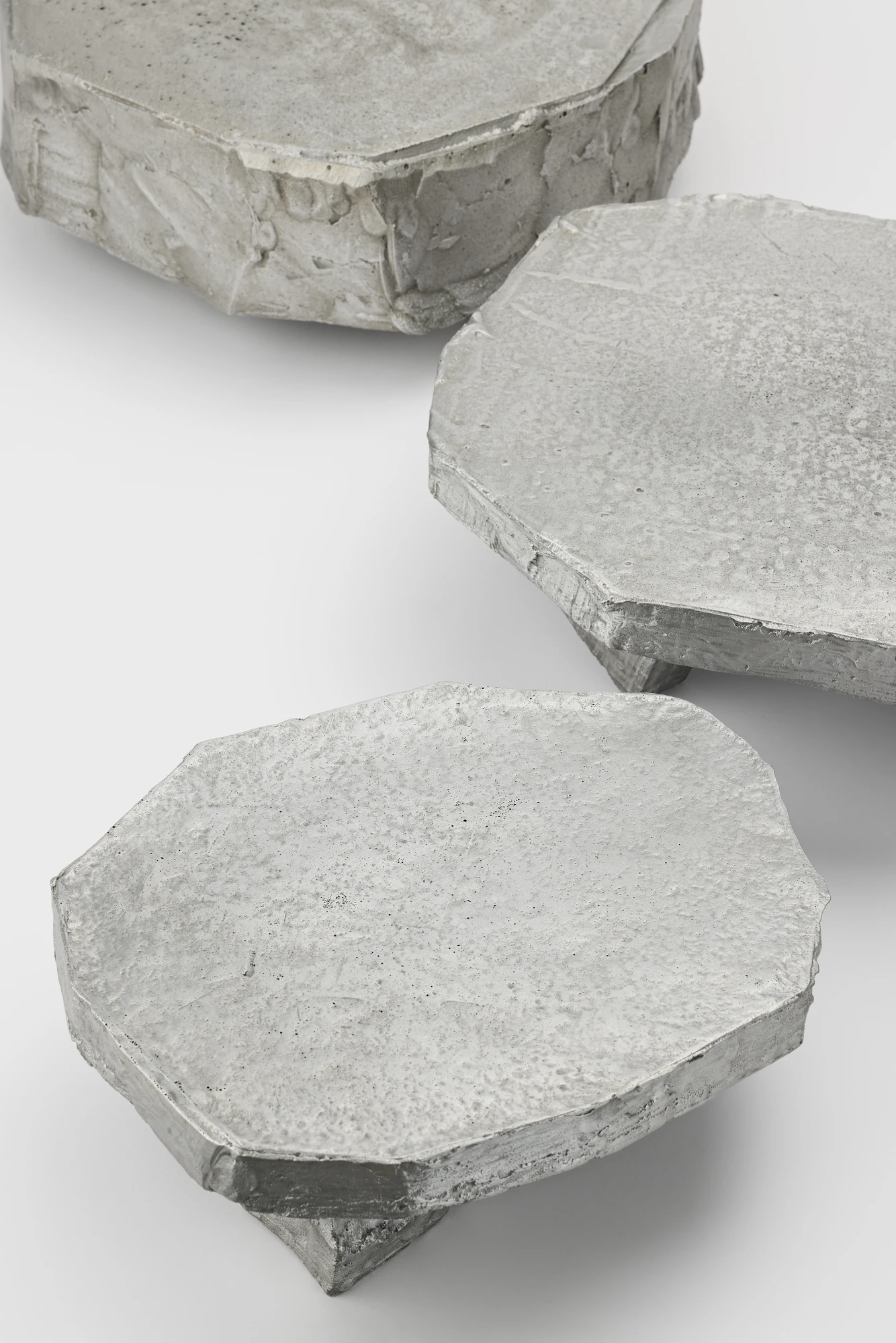 Lying on the floor by StudioFA, photographed by Yongin Myoung — Three faceted tops seen close and from above, their edges irregular and the casting texture visible across each surface.