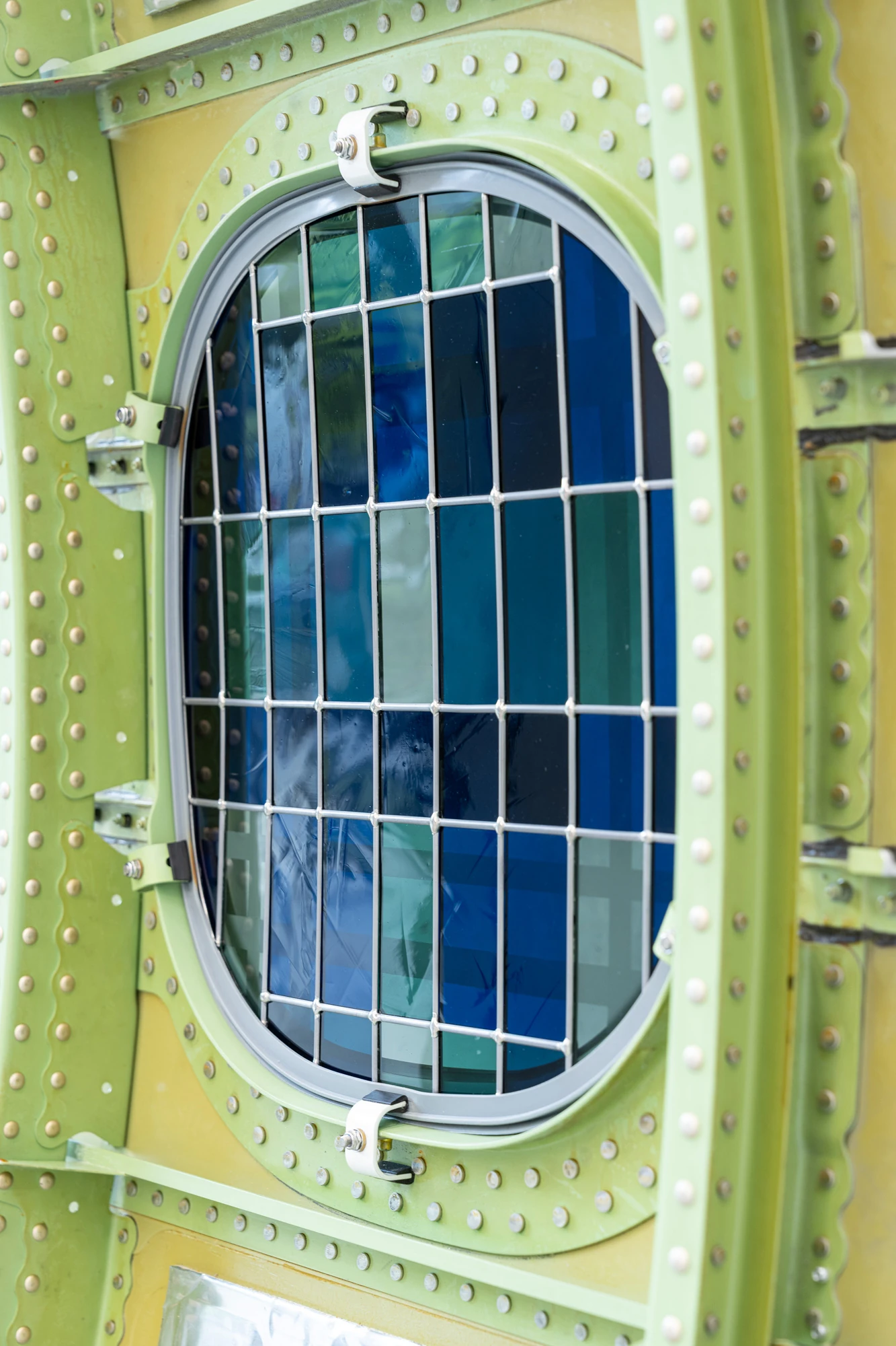 Addresses Without Names by Ju Young Kim, photographed by Dirk Tacke — A close view of She always sat on the same side of the table, its oval pane of blue, teal and green sanded glass gridded with lead against the green riveted airframe.