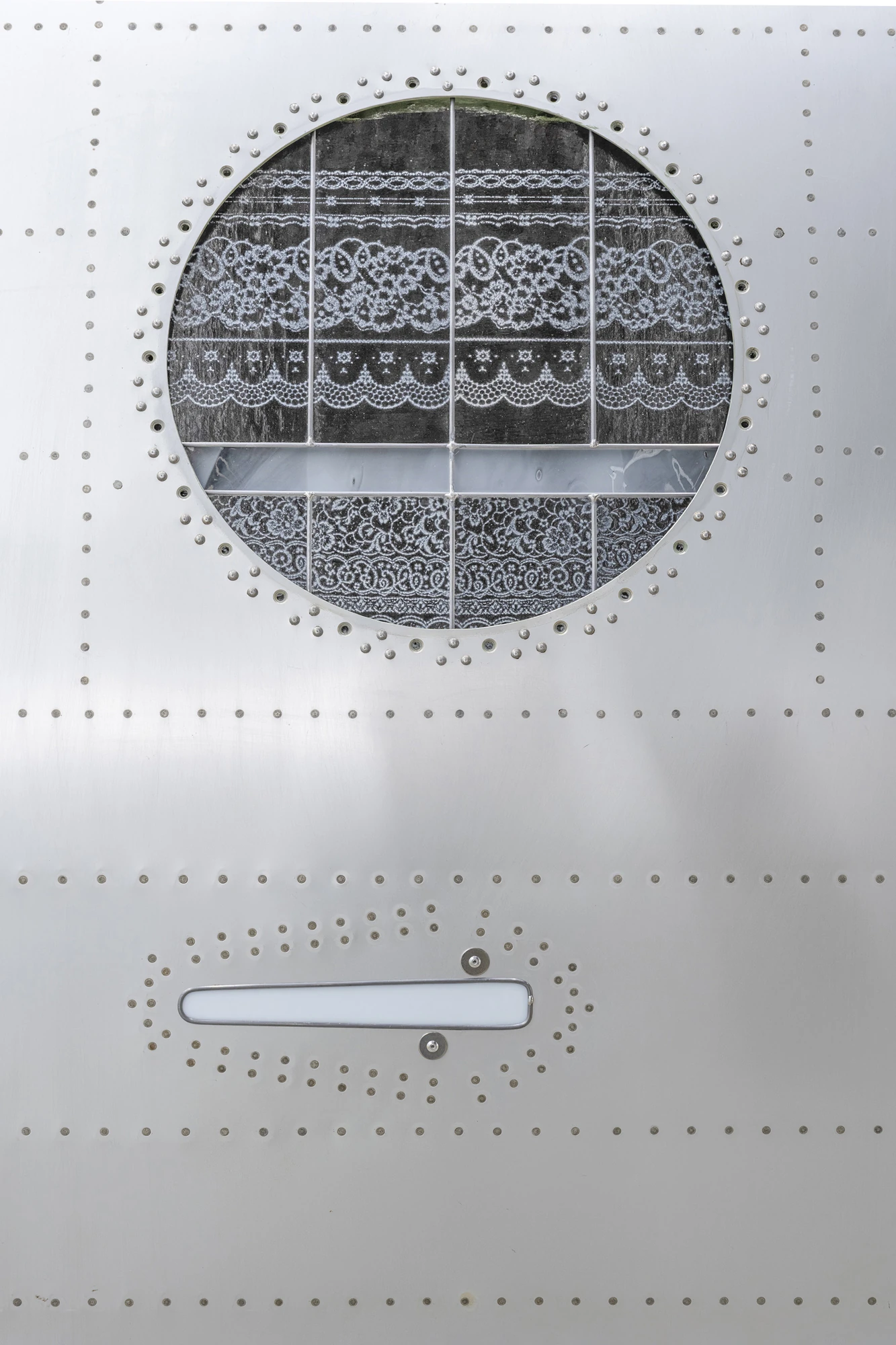 Addresses Without Names by Ju Young Kim, photographed by Dirk Tacke — A detail of Names behind the sun-faded plastic, its round window filled with printed glass carrying a black-and-white lace pattern and assembled with lead and tin in the riveted skin.