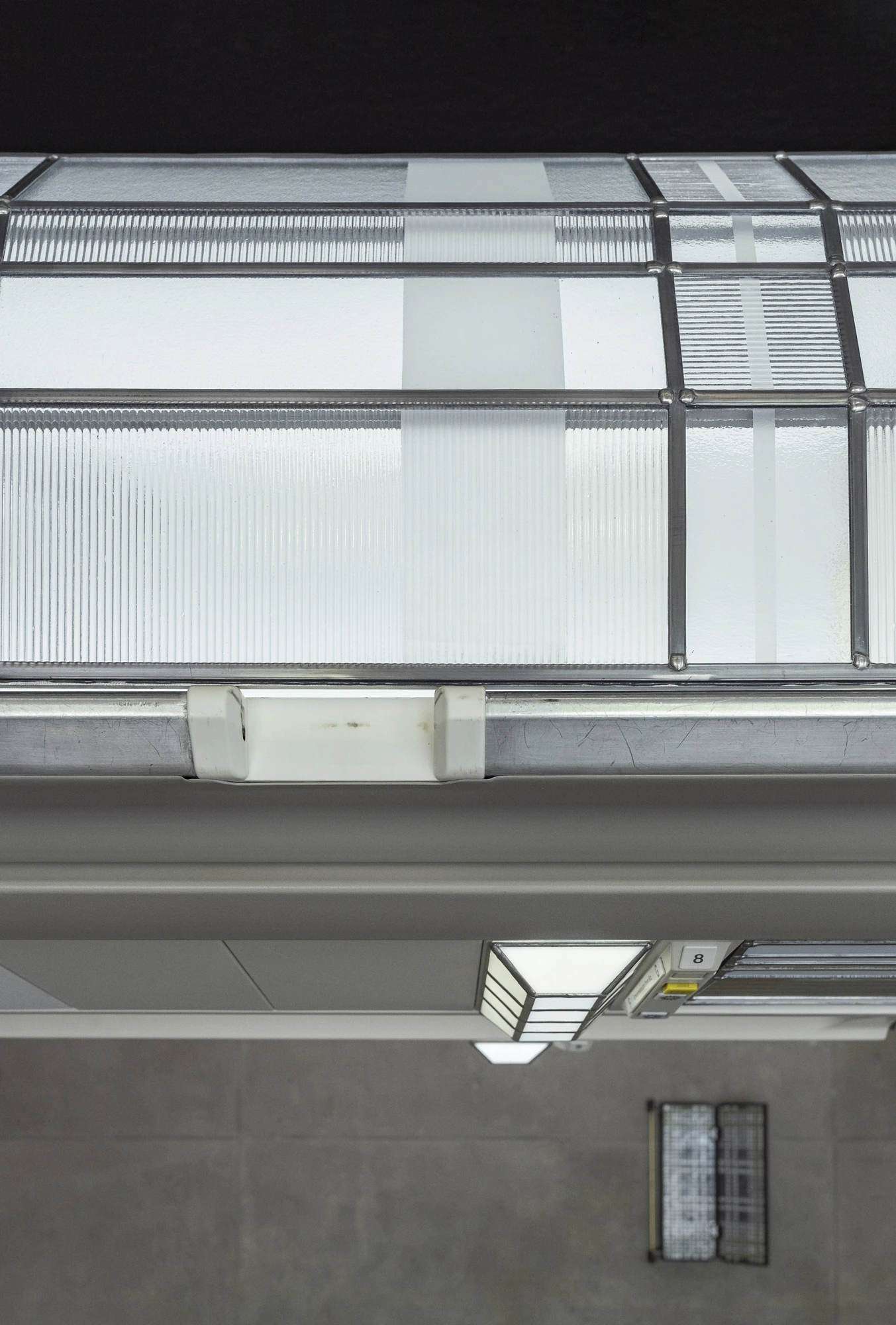 Addresses Without Names by Ju Young Kim, photographed by Dirk Tacke — A detail of the overhead compartment, its ribbed and frosted leaded glass beside a single Art Deco-style reading light marked with a seat number.
