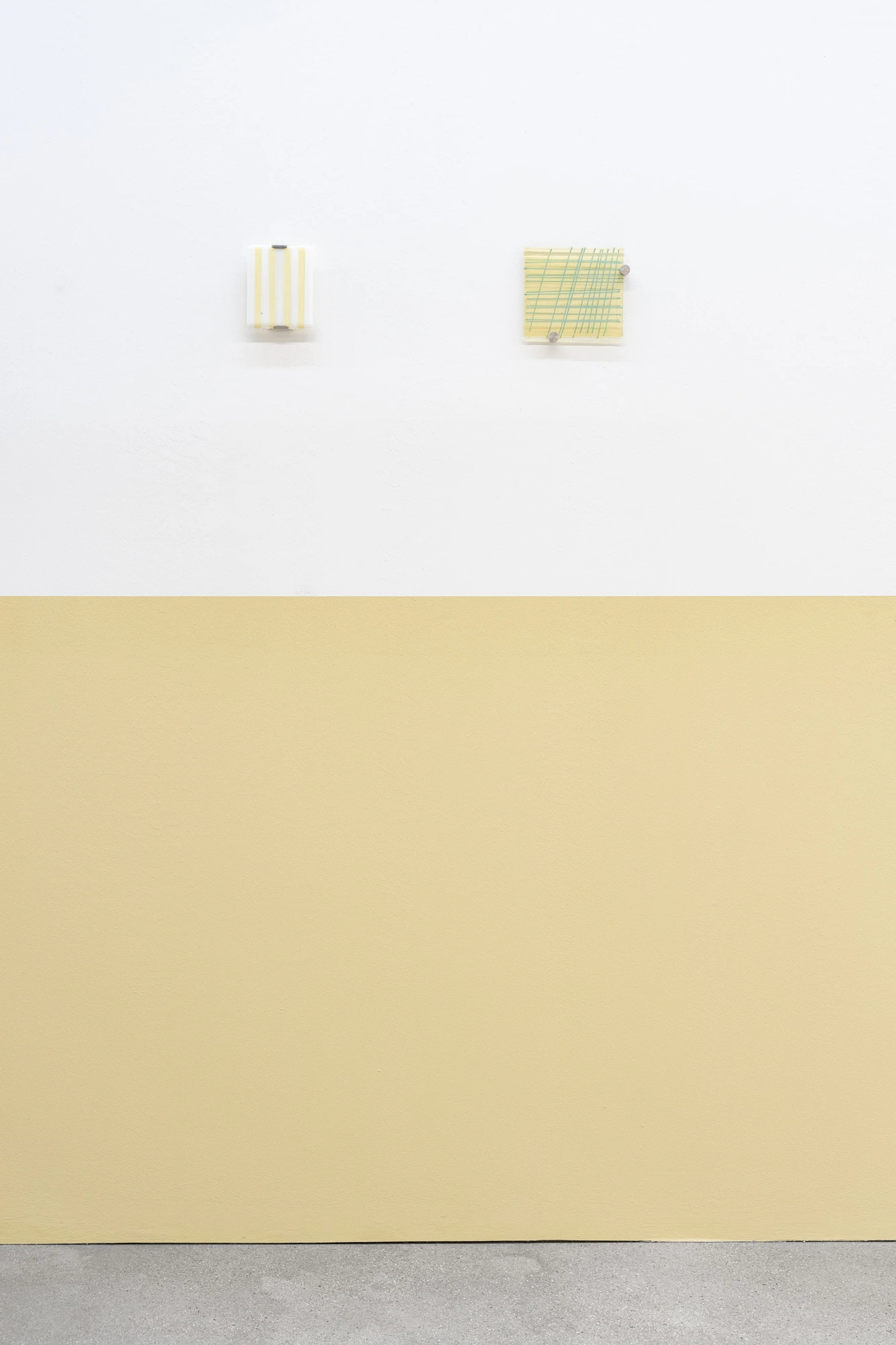 Addresses Without Names by Ju Young Kim, photographed by Dirk Tacke — Two small glass panels on the white-and-ochre wall, one striped in pale yellow and the other a green plaid drawn over yellow, each held off the wall on steel pins.