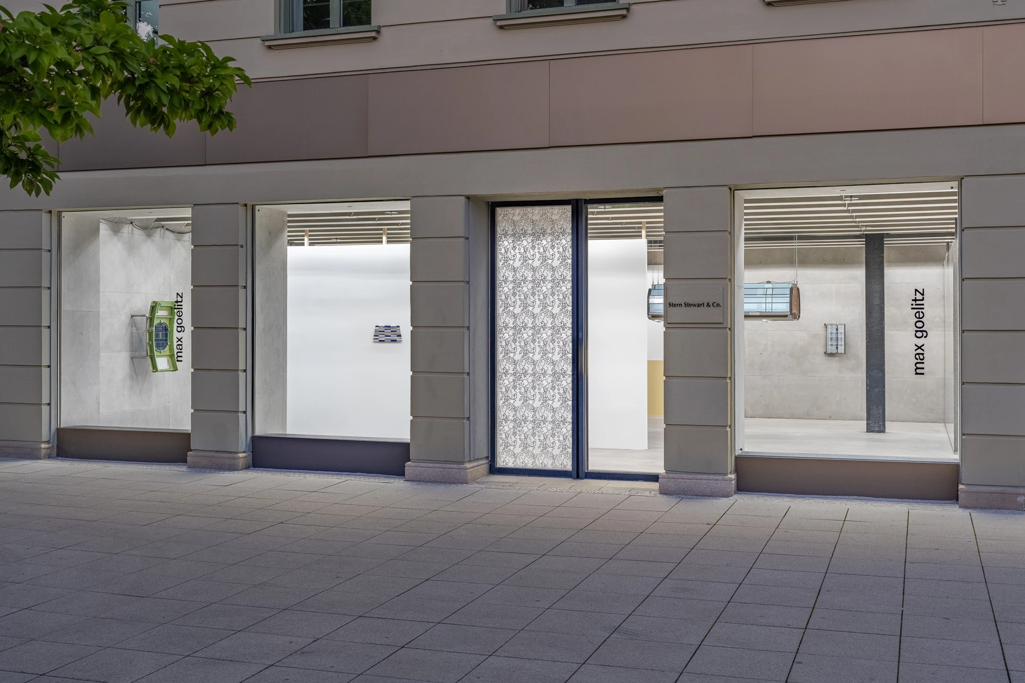 Addresses Without Names by Ju Young Kim, photographed by Dirk Tacke — The street front of max goelitz on Maximiliansplatz, its windows lettered with the gallery name, a lace-printed film on the entrance door and glass works shown in the vitrines.