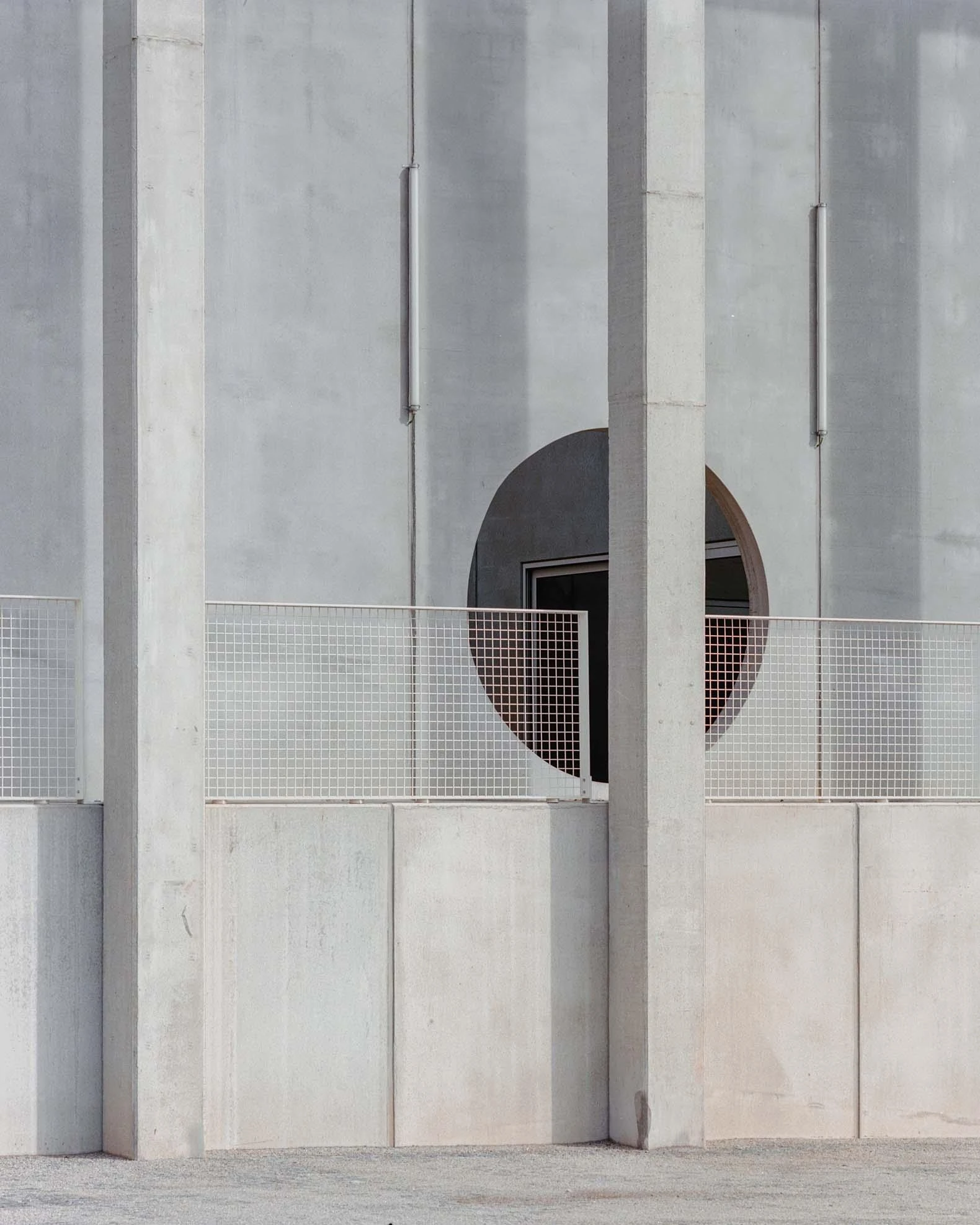 Corcet Headquarters by Nuno M. Sousa, photographed by Federico Farinatti, Francisco Ascensão — A full circle is cut clean through the wall behind the gallery, a pillar splitting the opening and a mesh rail running across its base.