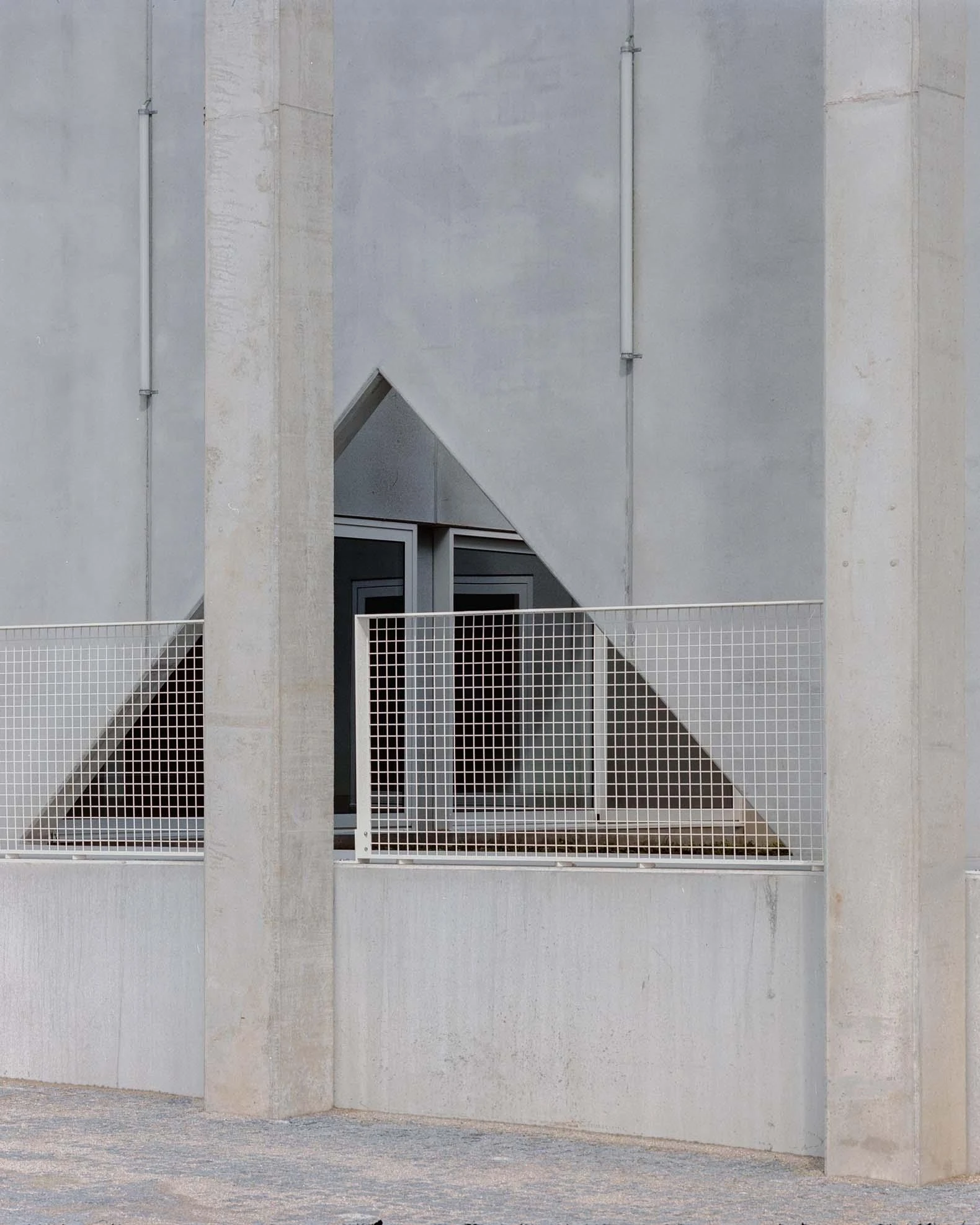 Corcet Headquarters by Nuno M. Sousa, photographed by Federico Farinatti, Francisco Ascensão — Two pillars frame a triangular notch cut into the wall, where a mesh guardrail crosses in front of a recessed window.