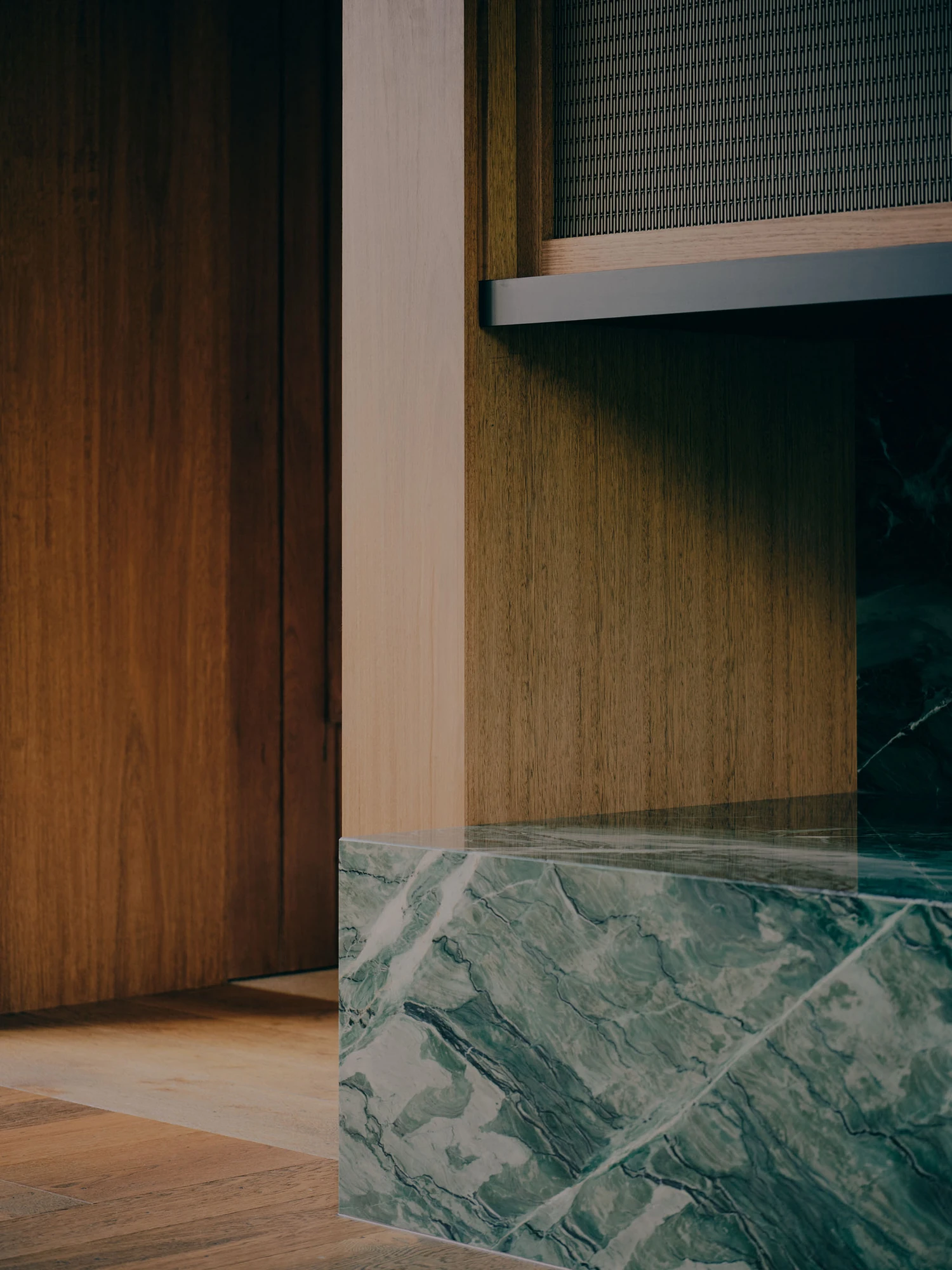 The Farm by Wolveridge Architects, photographed by Jack Carlin — A close view of the green-veined stone hearth block meeting timber veneer cabinetry and a slim grey steel shelf, the pale timber floor running beneath.