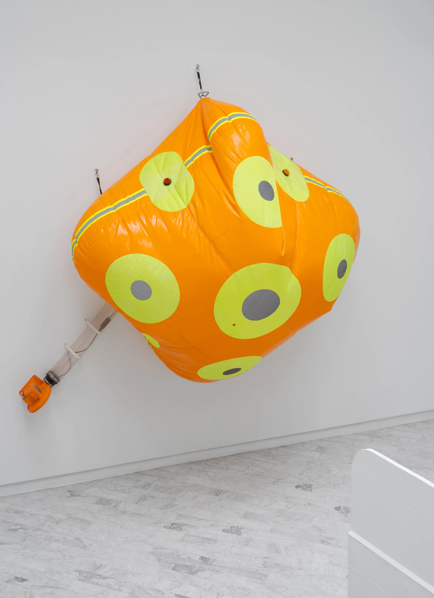 Walls at the World’s End by Louis Morlæ, photographed by David Stjernholm — Close vertical view of the orange inflatable bulging off the wall, its hazard-yellow band and yellow discs catching the light, suspended on rigging straps with a ribbed tube…