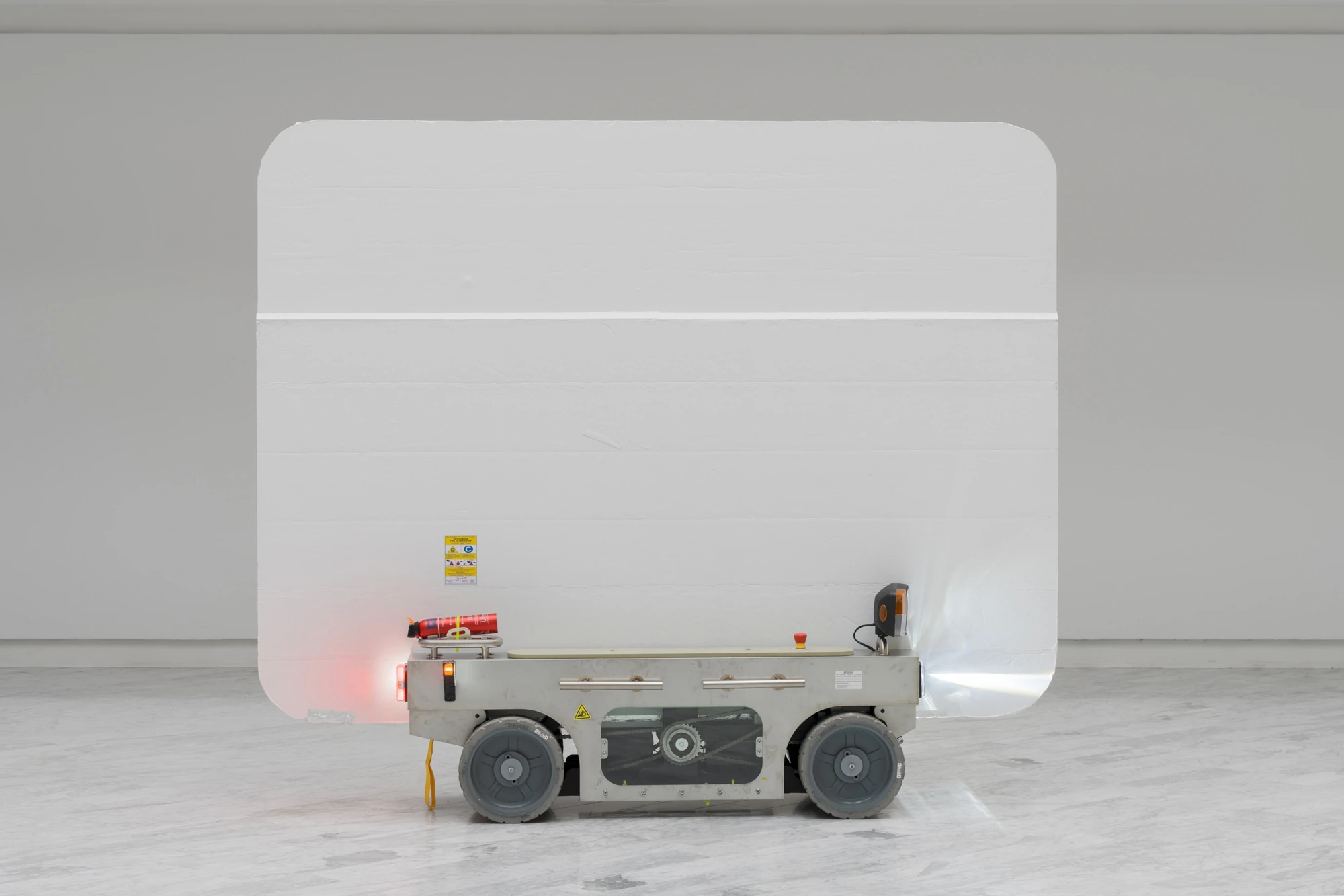 Walls at the World’s End by Louis Morlæ, photographed by David Stjernholm — The panel-cart in side profile, its white panel lowered, the grey steel chassis and chunky wheels exposed, an amber beacon and red lamp glowing on the marble floor.