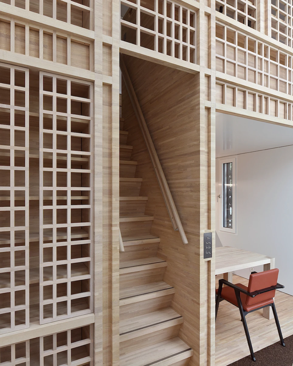 Writers' Cabins at the Jan Michalski Foundation by Kengo Kuma, ELEMENTAL, MK27 and Others, photographed by Leo Fabrizio, Tonatiuh Ambrosetti — Pale timber lines the interior of Décosterd's cabin, where a stair with metal-nosed treads climbs past gridded…