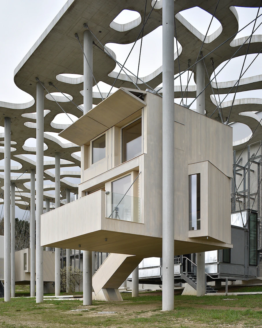 Writers' Cabins at the Jan Michalski Foundation by Kengo Kuma, ELEMENTAL, MK27 and Others, photographed by Leo Fabrizio, Tonatiuh Ambrosetti — Fuhrimann and Hächler's pale accoya cabin cantilevers a balcony behind a glass balustrade, braced by an angled…