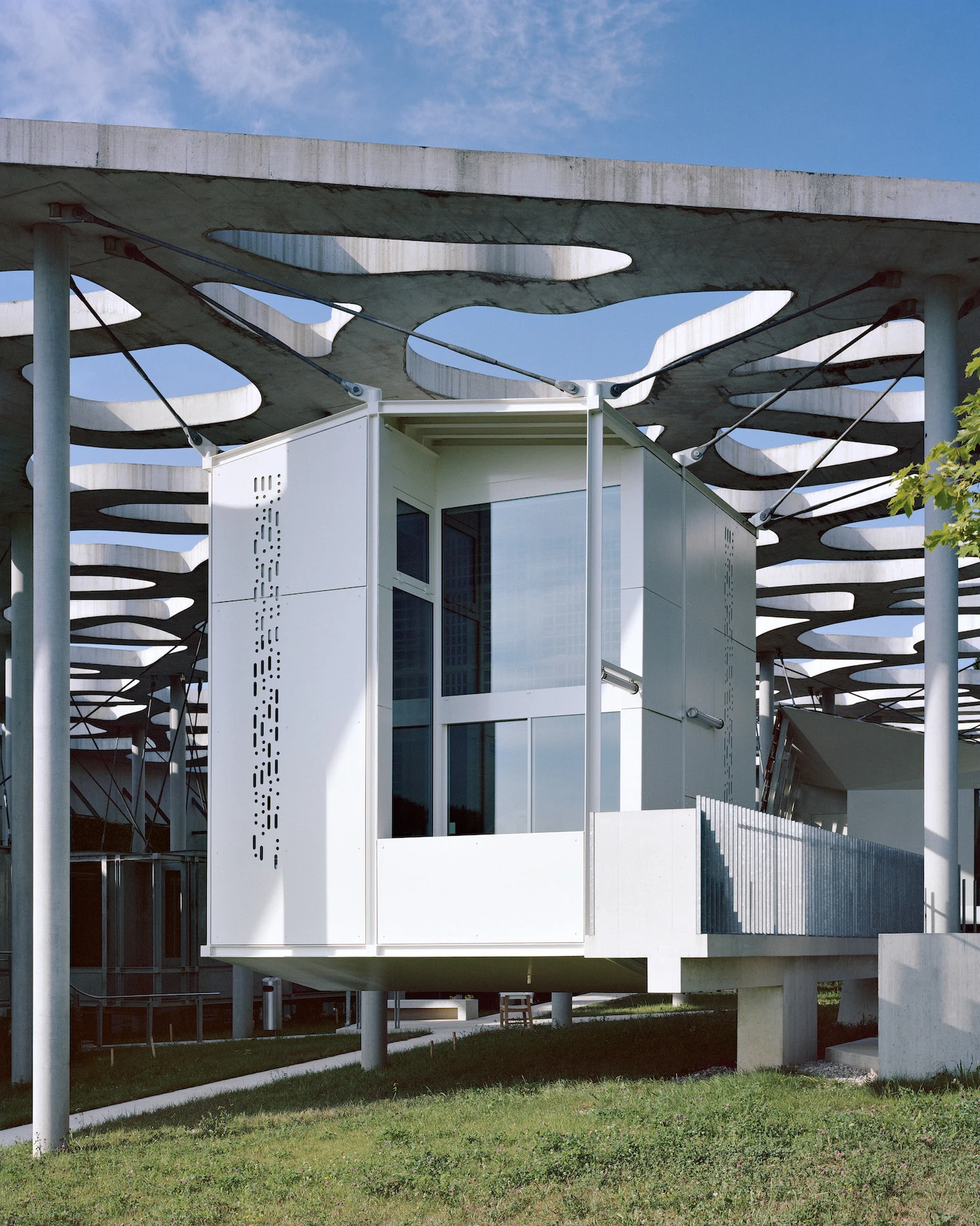 Writers' Cabins at the Jan Michalski Foundation by Kengo Kuma, ELEMENTAL, MK27 and Others, photographed by Leo Fabrizio, Tonatiuh Ambrosetti — Under the board-marked concrete canopy and its organic voids, Décosterd's white galvanised-steel panels carry…