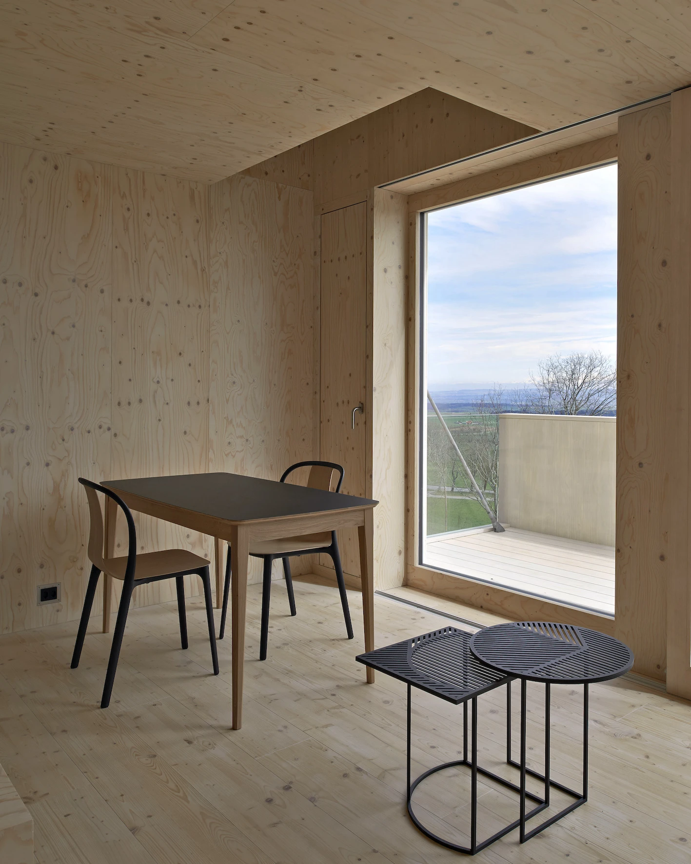 Writers' Cabins at the Jan Michalski Foundation by Kengo Kuma, ELEMENTAL, MK27 and Others, photographed by Leo Fabrizio, Tonatiuh Ambrosetti — Knotty pine lines the interior of Fuhrimann and Hächler's cabin, a full-height window opening to a timber…