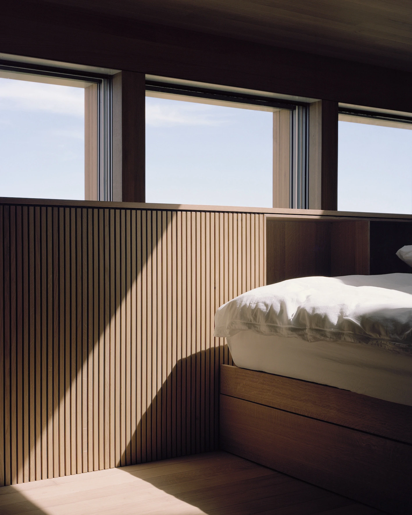 Writers' Cabins at the Jan Michalski Foundation by Kengo Kuma, ELEMENTAL, MK27 and Others, photographed by Leo Fabrizio, Tonatiuh Ambrosetti — Inside Studio MK27's cabin, an oak-batten screen wraps the nested inner volume beside a low bed in white…