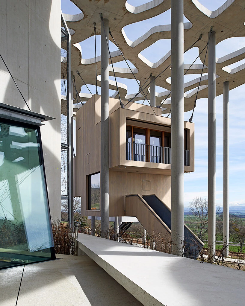 Writers' Cabins at the Jan Michalski Foundation by Kengo Kuma, ELEMENTAL, MK27 and Others, photographed by Leo Fabrizio, Tonatiuh Ambrosetti — Rintala Eggertsson's pale timber cabin stacks a balcony over a lower window beneath the canopy, a glazed stair…