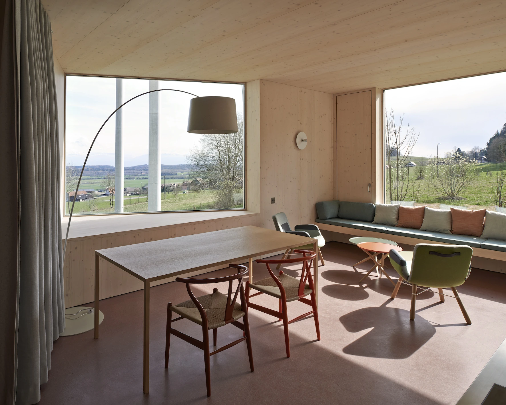 Writers' Cabins at the Jan Michalski Foundation by Kengo Kuma, ELEMENTAL, MK27 and Others, photographed by Leo Fabrizio, Tonatiuh Ambrosetti — Schaub Zwicky's single-level room lines pale spruce over a terracotta floor, wishbone chairs at a slim table…