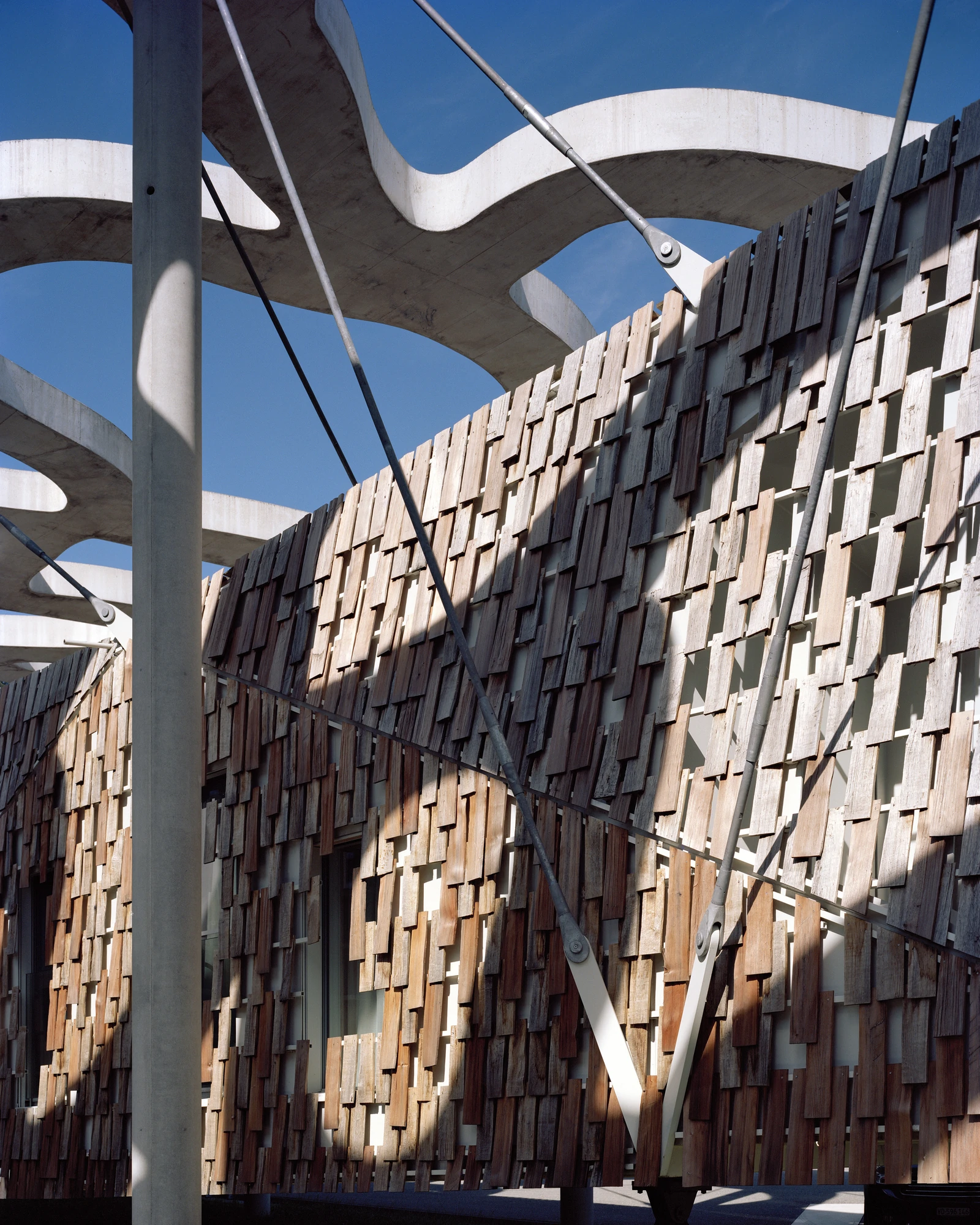 Writers' Cabins at the Jan Michalski Foundation by Kengo Kuma, ELEMENTAL, MK27 and Others, photographed by Leo Fabrizio, Tonatiuh Ambrosetti — A checkerboard of hand-cut oak and larch shingles, left to weather over white steel, covers Kengo Kuma &…